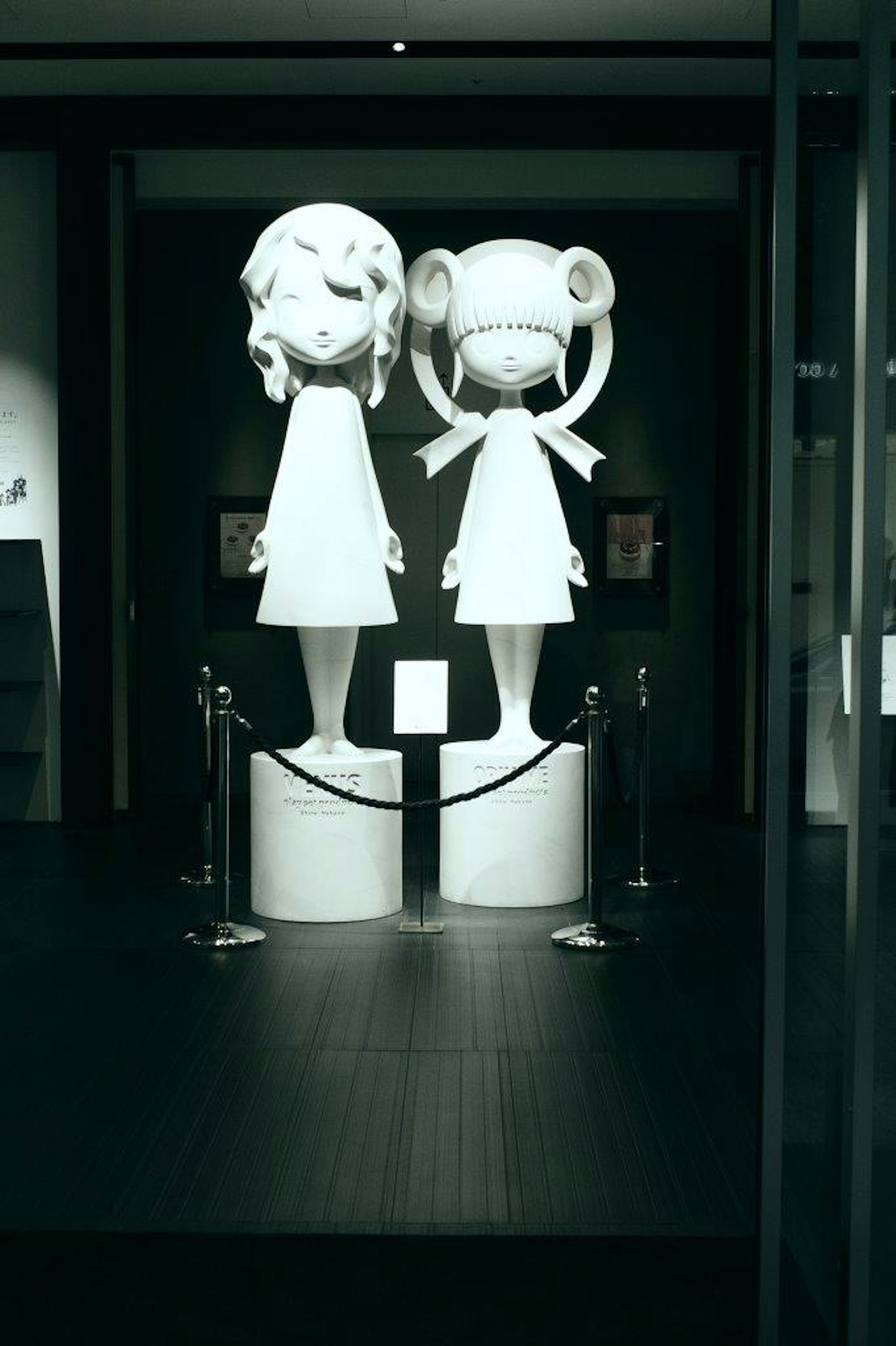 Two white sculptures of girls standing side by side