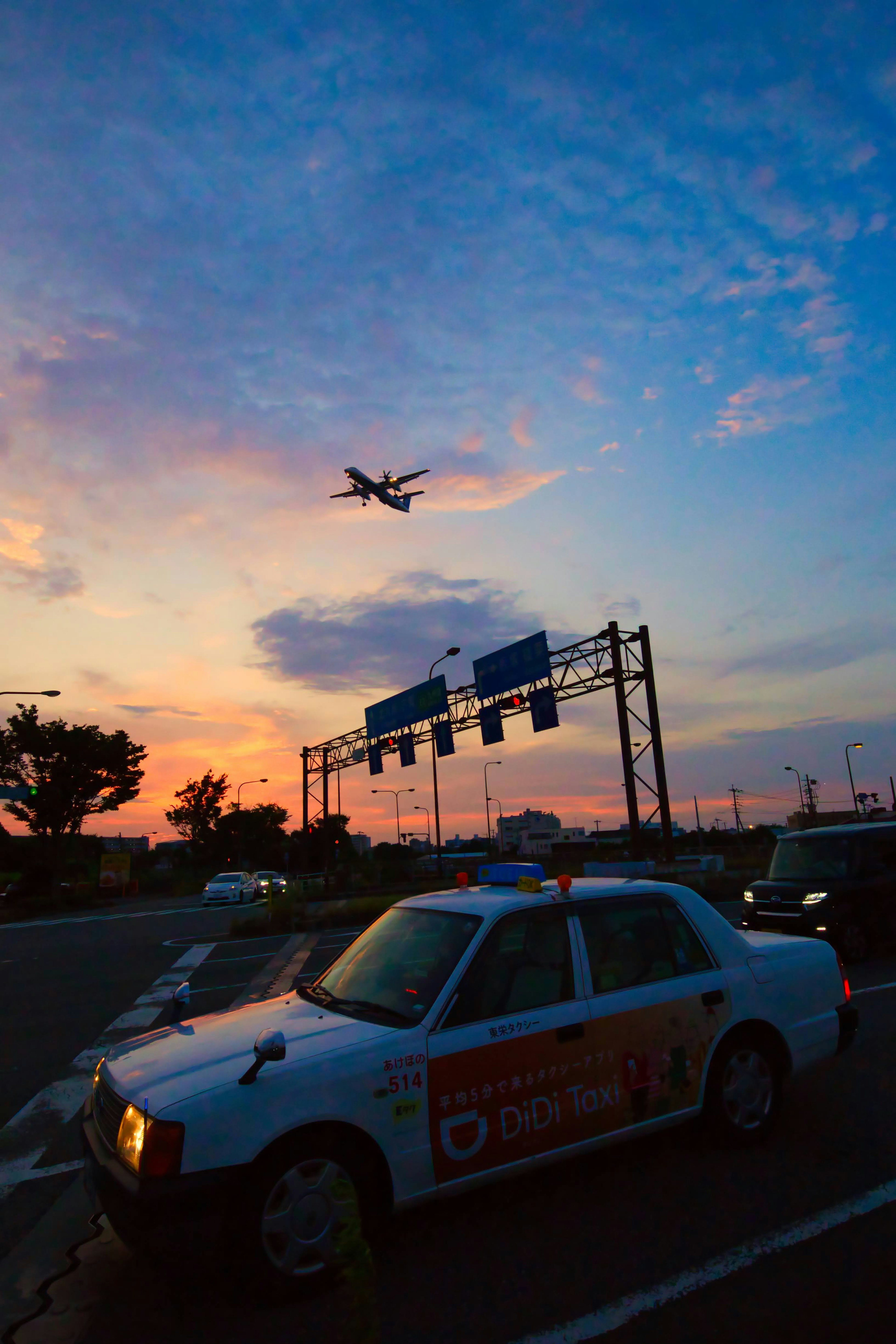 Taxi estacionado al lado de la carretera con un avión volando en el cielo del atardecer