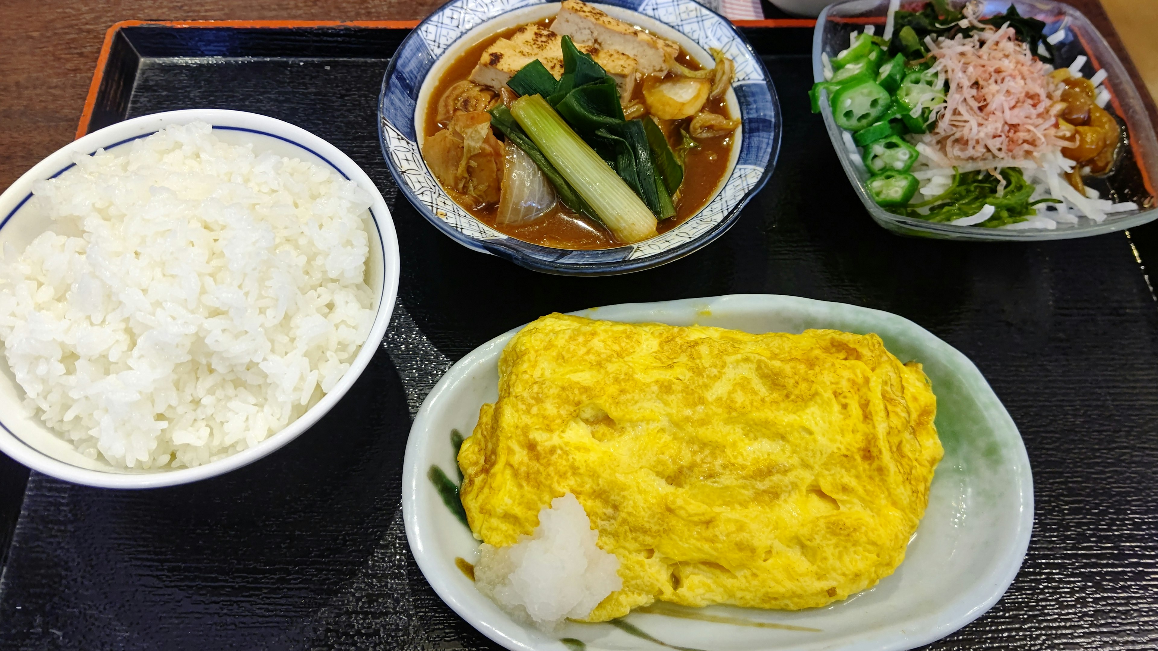 A Japanese meal featuring rice, an omelet, miso soup, and a salad