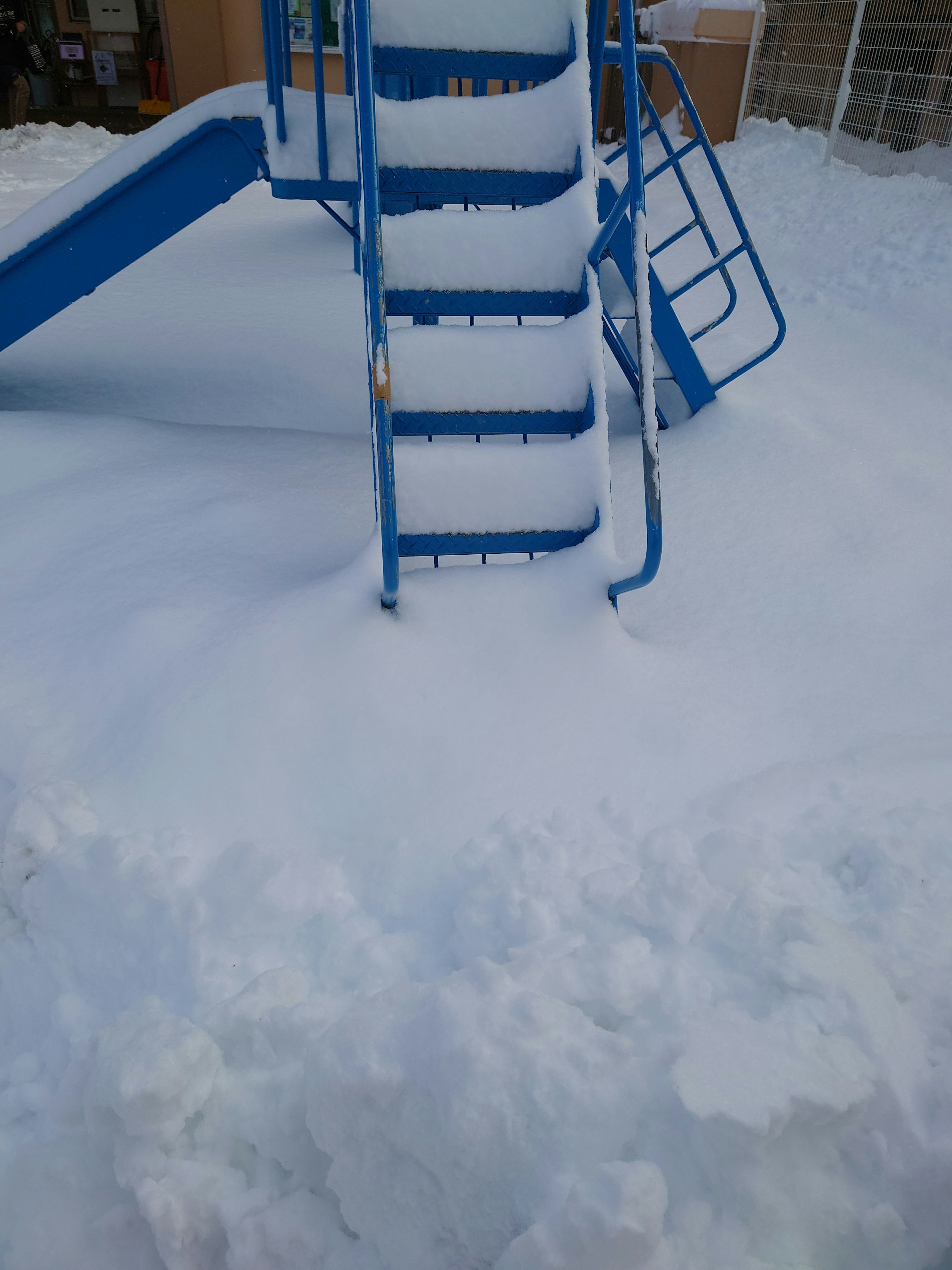 Blue slide partially buried in snow at a playground