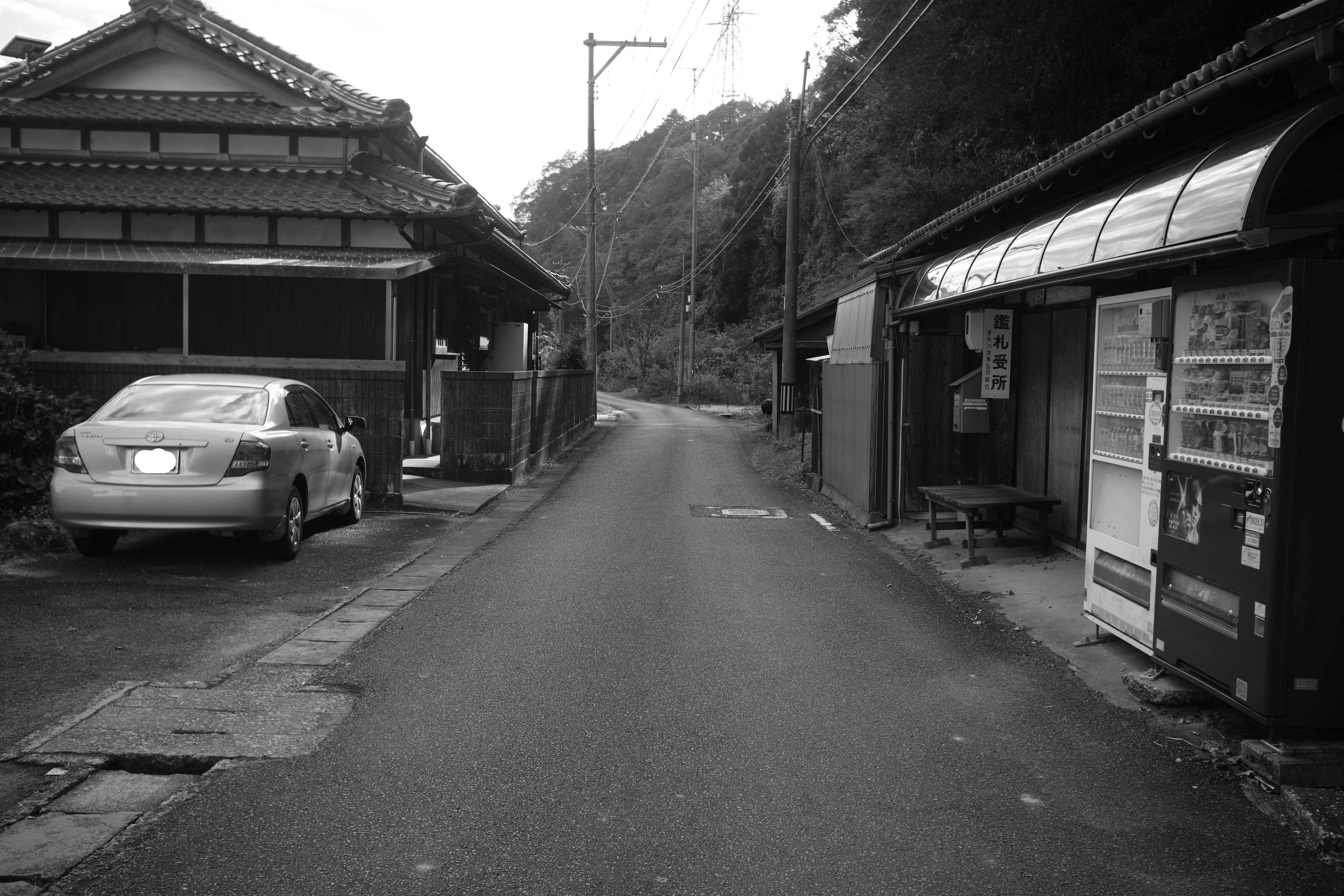 狭い道路に沿って古い日本の家と自動販売機がある風景