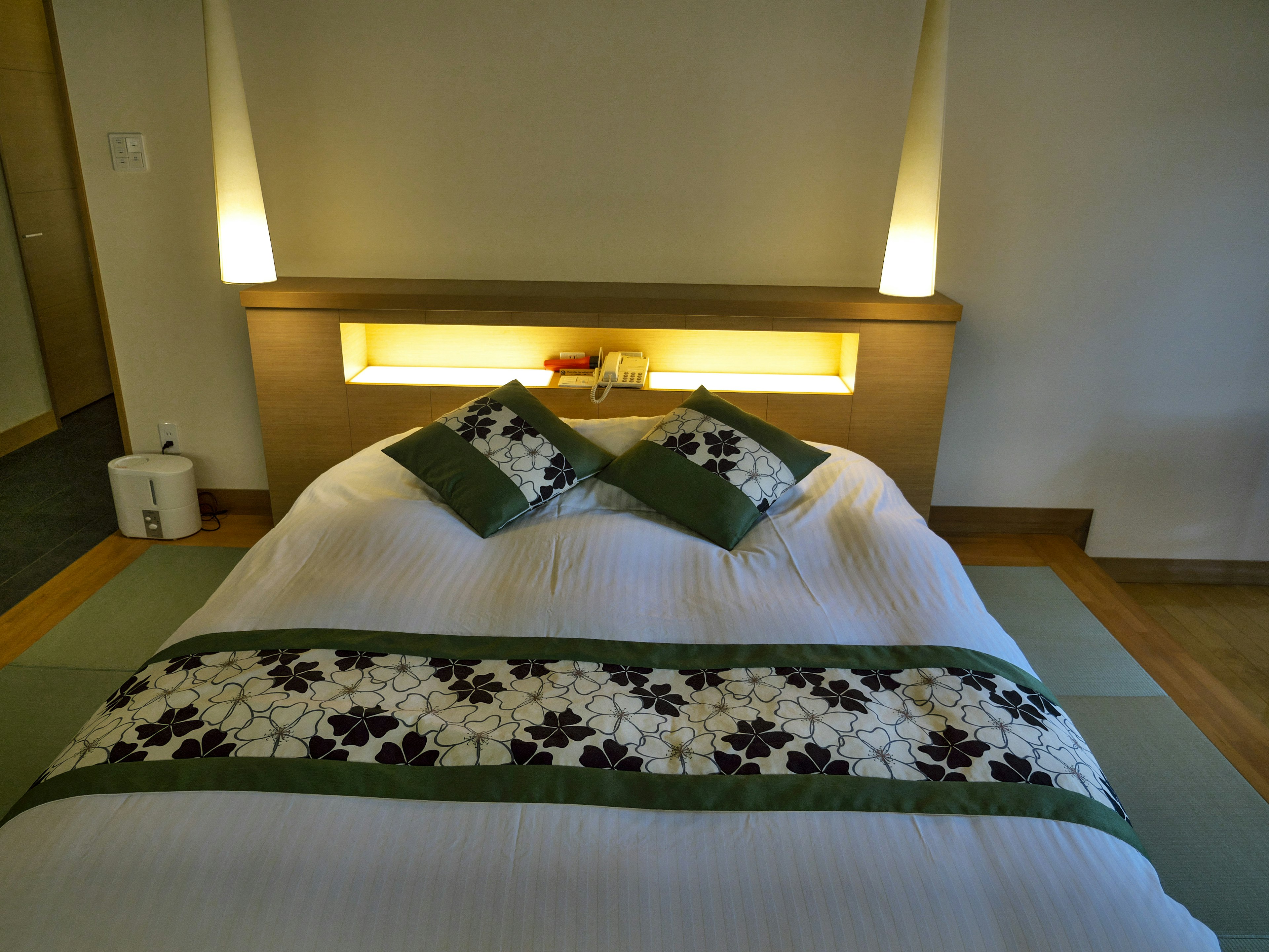 Modern and minimalist bedroom interior with white bedding and green decorative pillows illuminated headboard