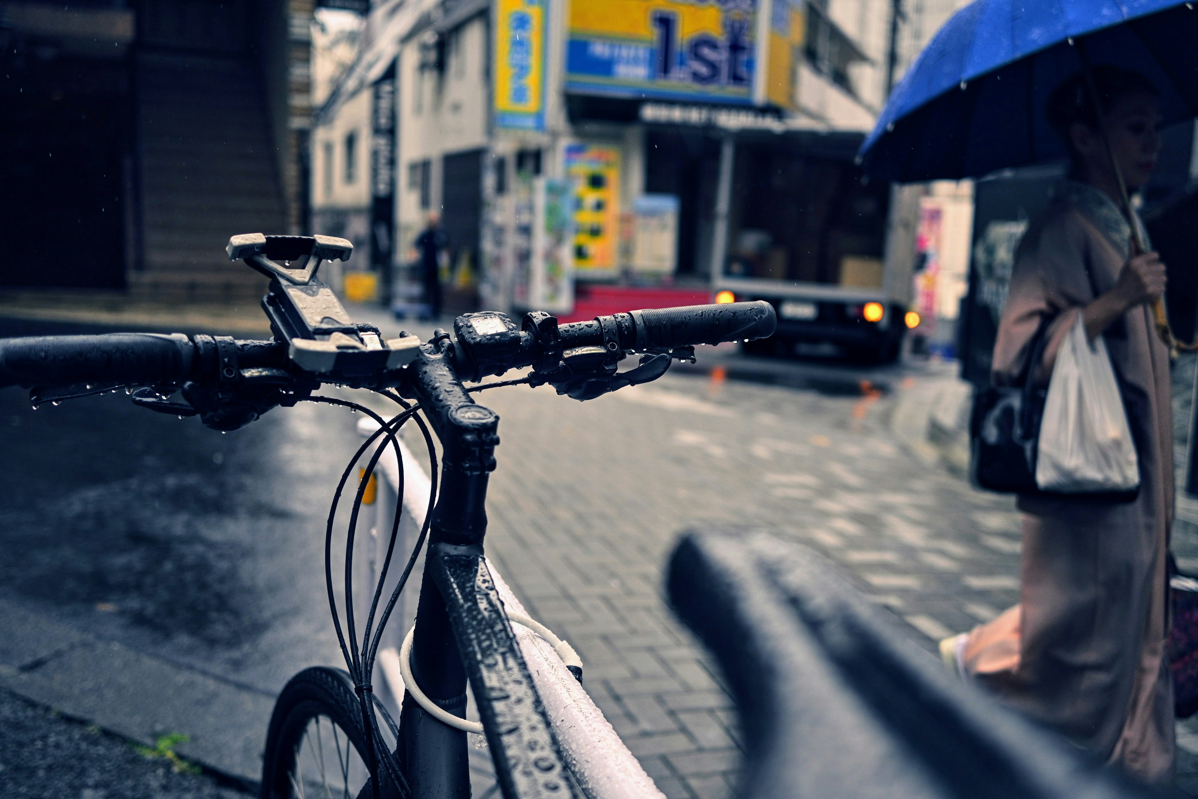 Wet bicycle handlebars with a pedestrian holding an umbrella in the rain