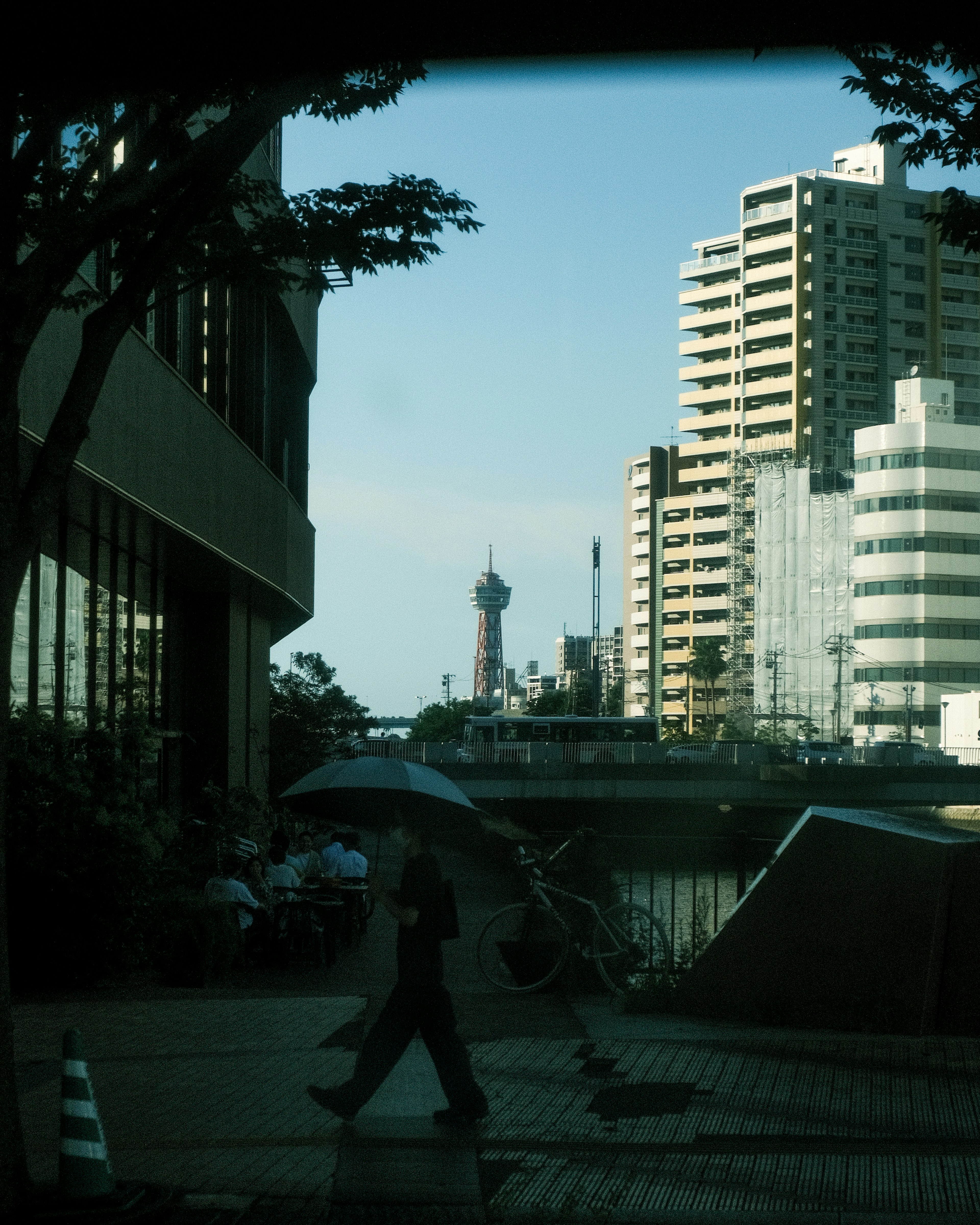 都市の風景に傘を持つ人物が歩いている画像ビルと橋が背景に見える