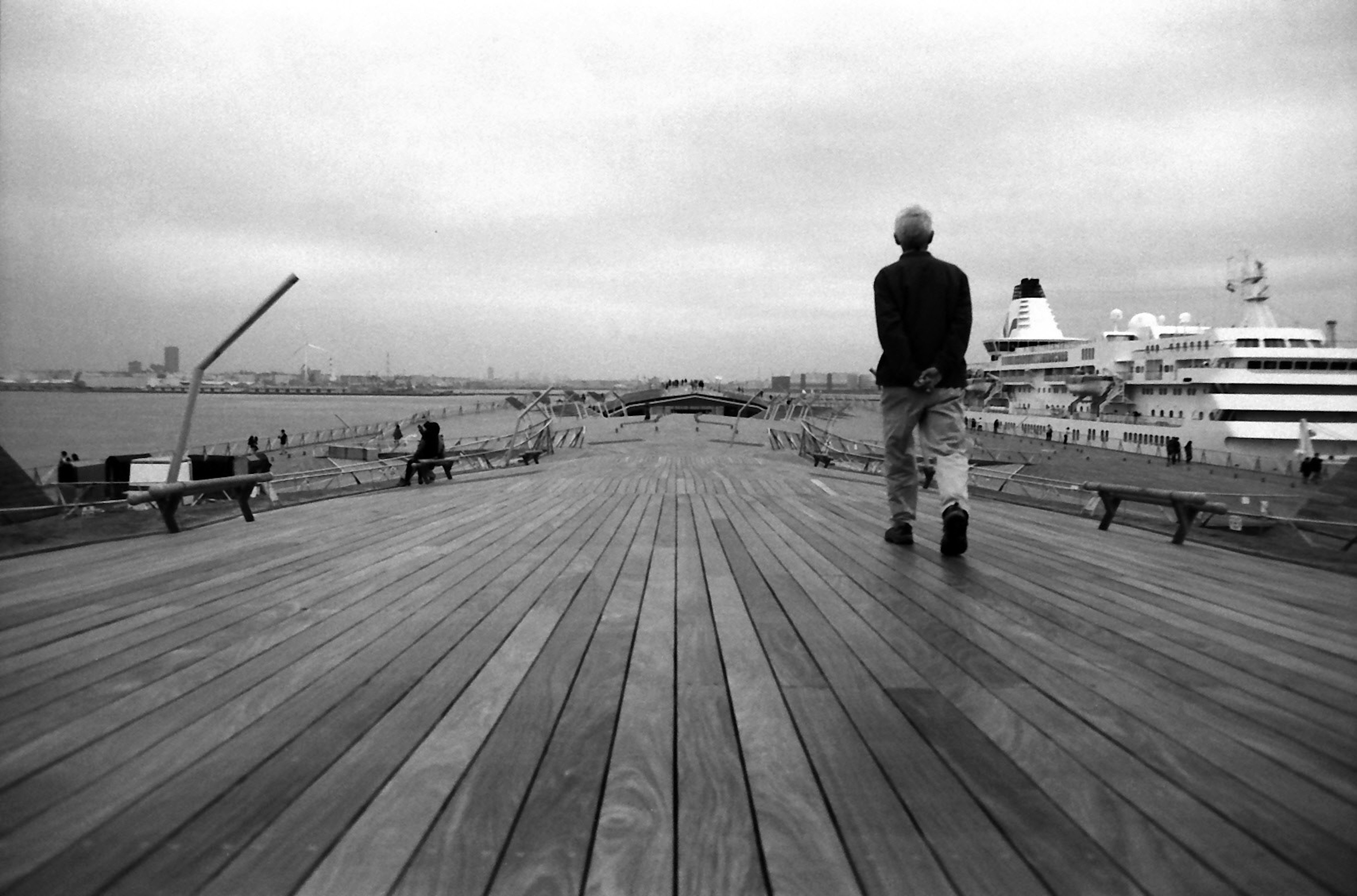 Un hombre caminando por un muelle de madera con un fondo en blanco y negro