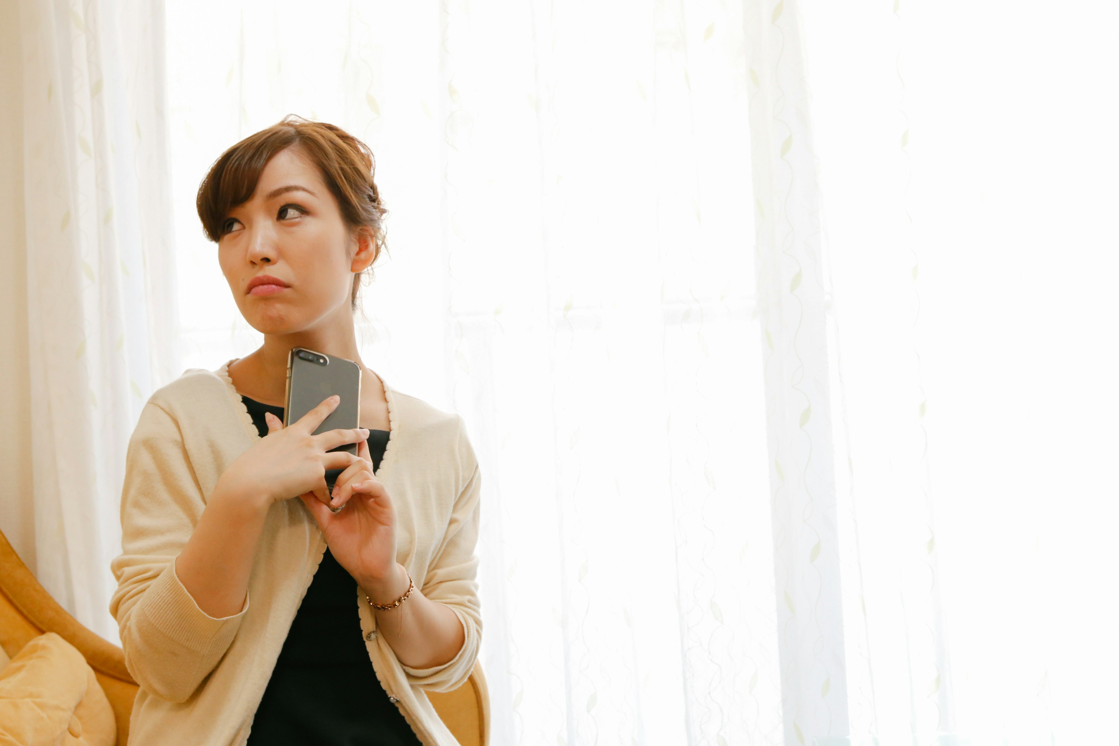 A woman holding a smartphone looking thoughtful