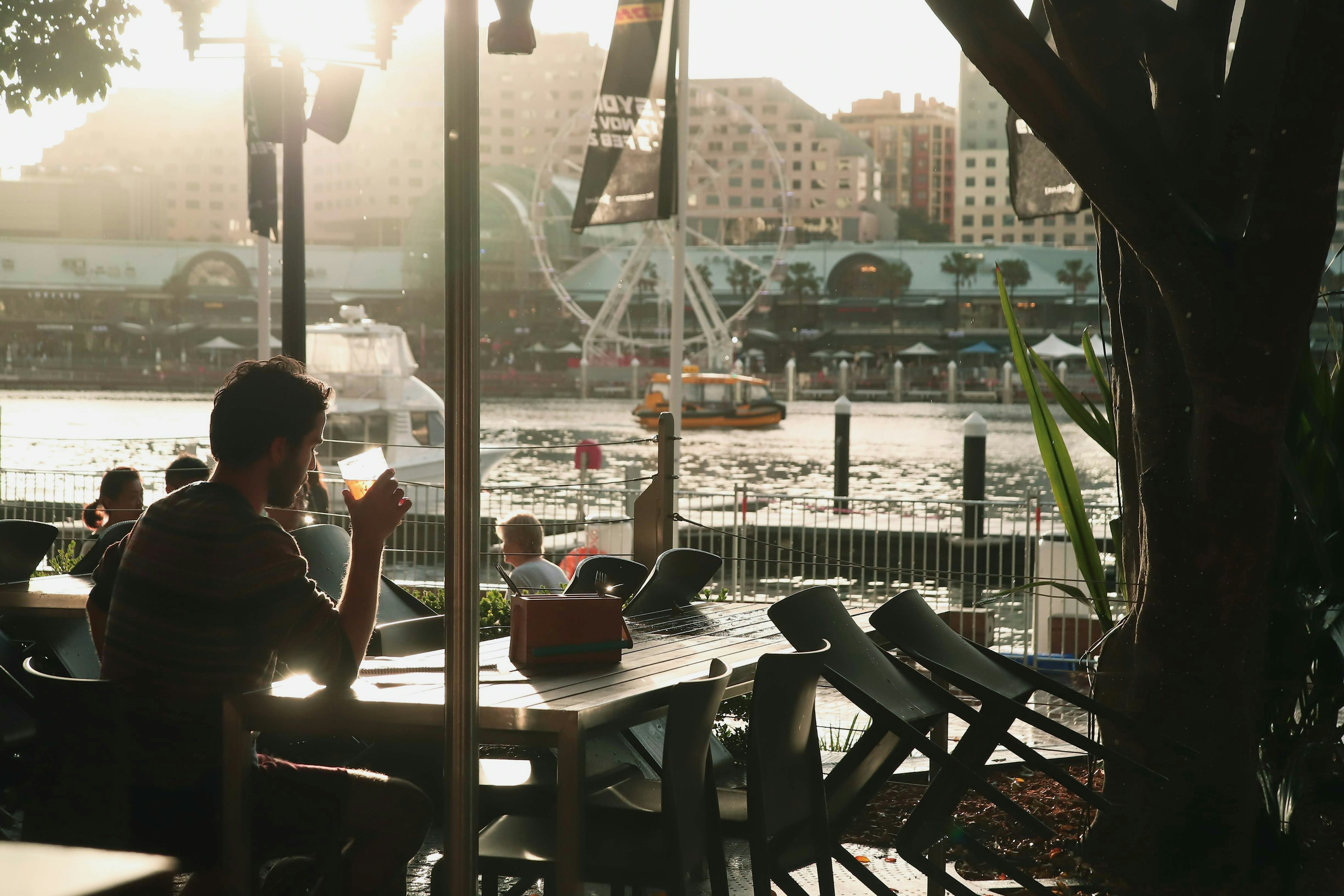 Personne appréciant une boisson dans un café au bord de la rivière avec une grande roue en arrière-plan