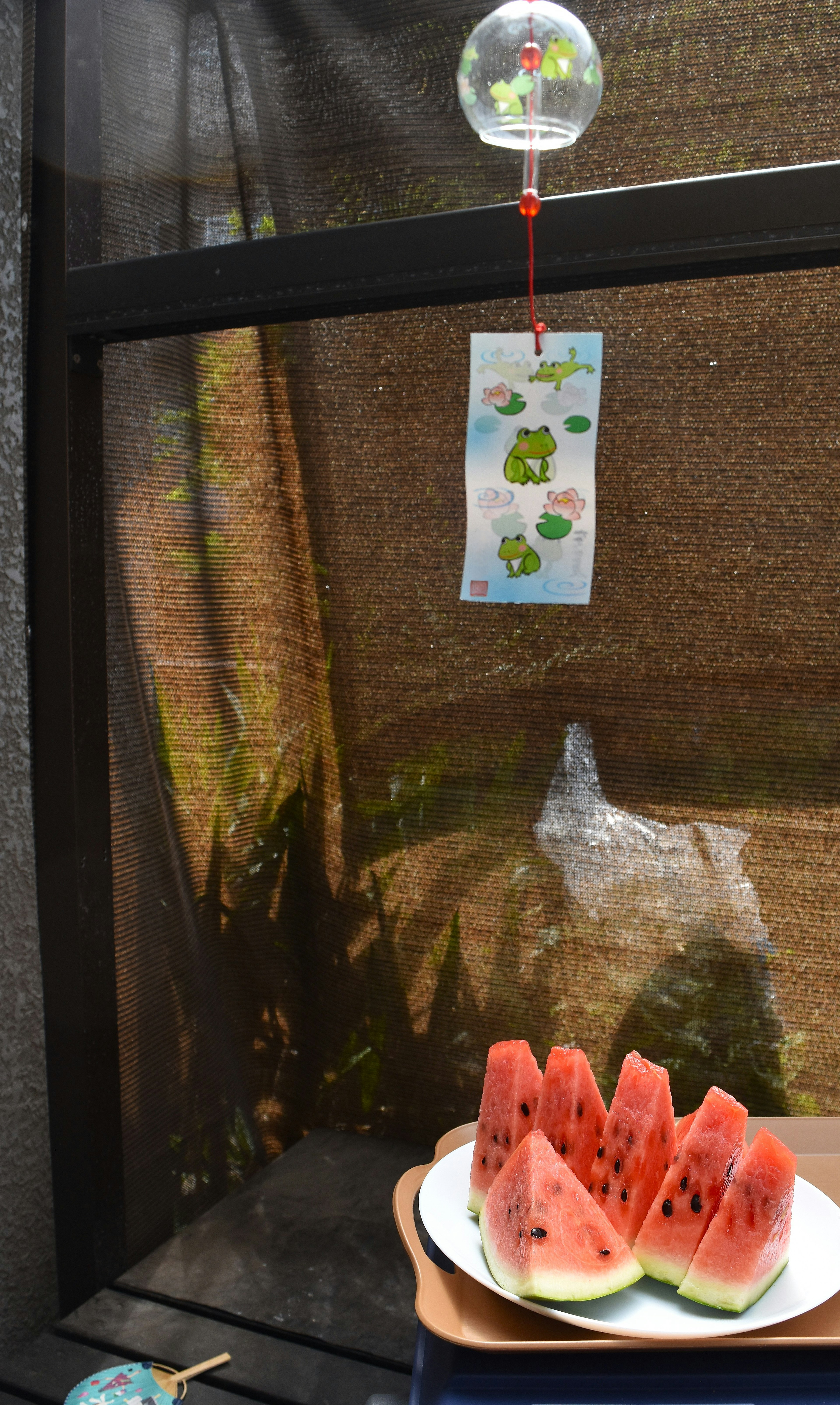 A plate of watermelon slices in a summer setting with a wind chime hanging above