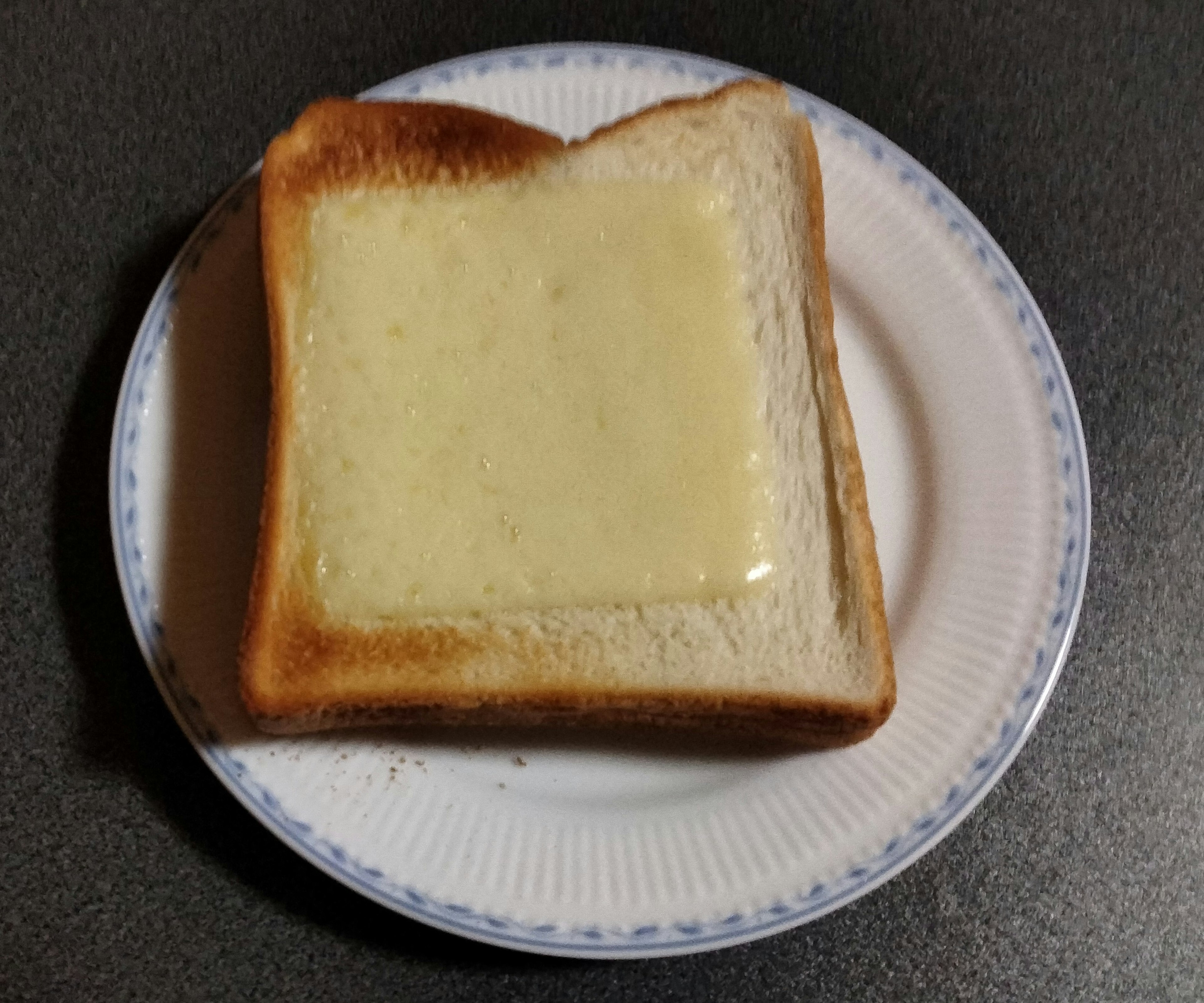 A slice of toasted bread topped with melted butter on a white plate