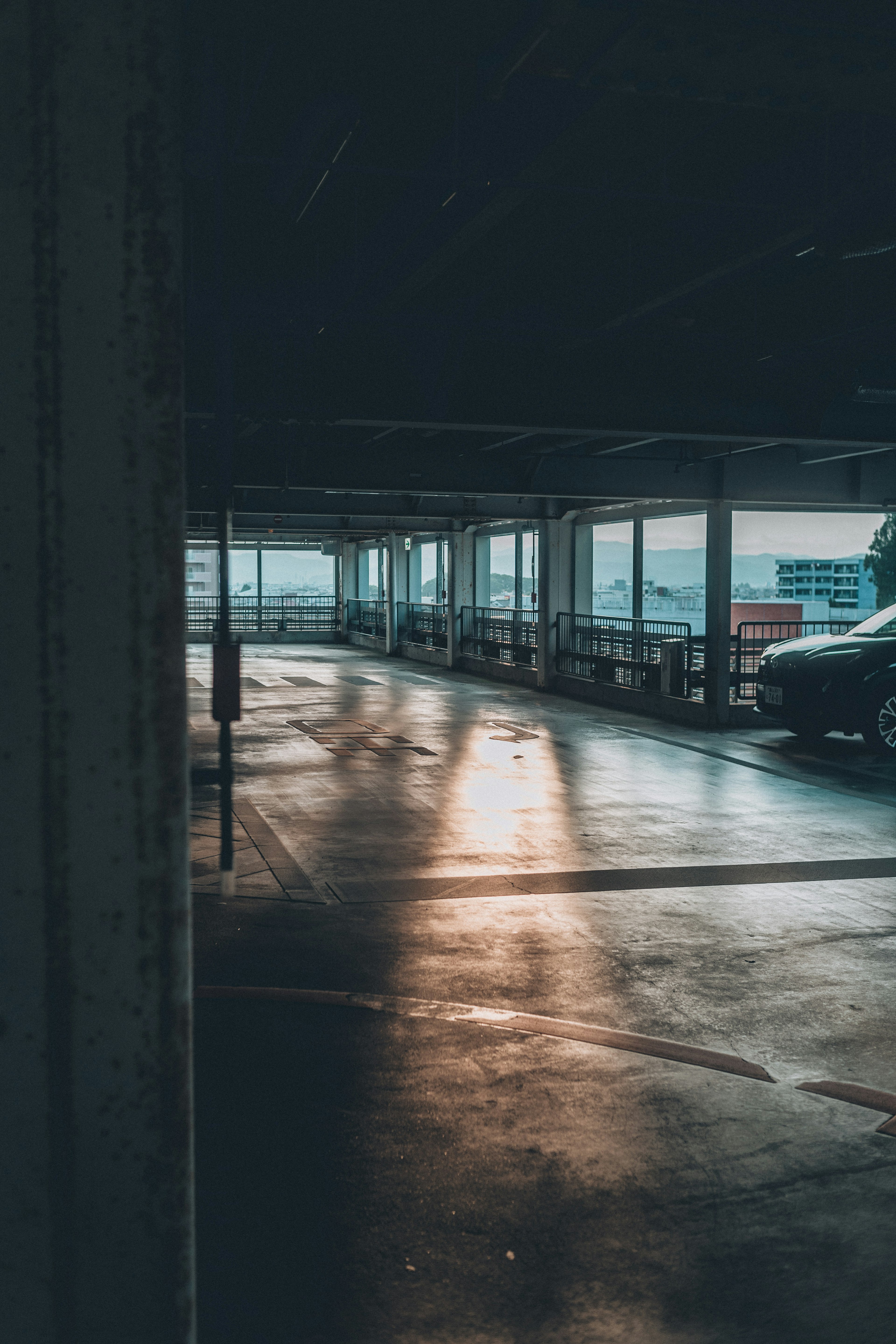 Garaje de estacionamiento débilmente iluminado con luz solar reflejándose en el suelo cerca de un coche