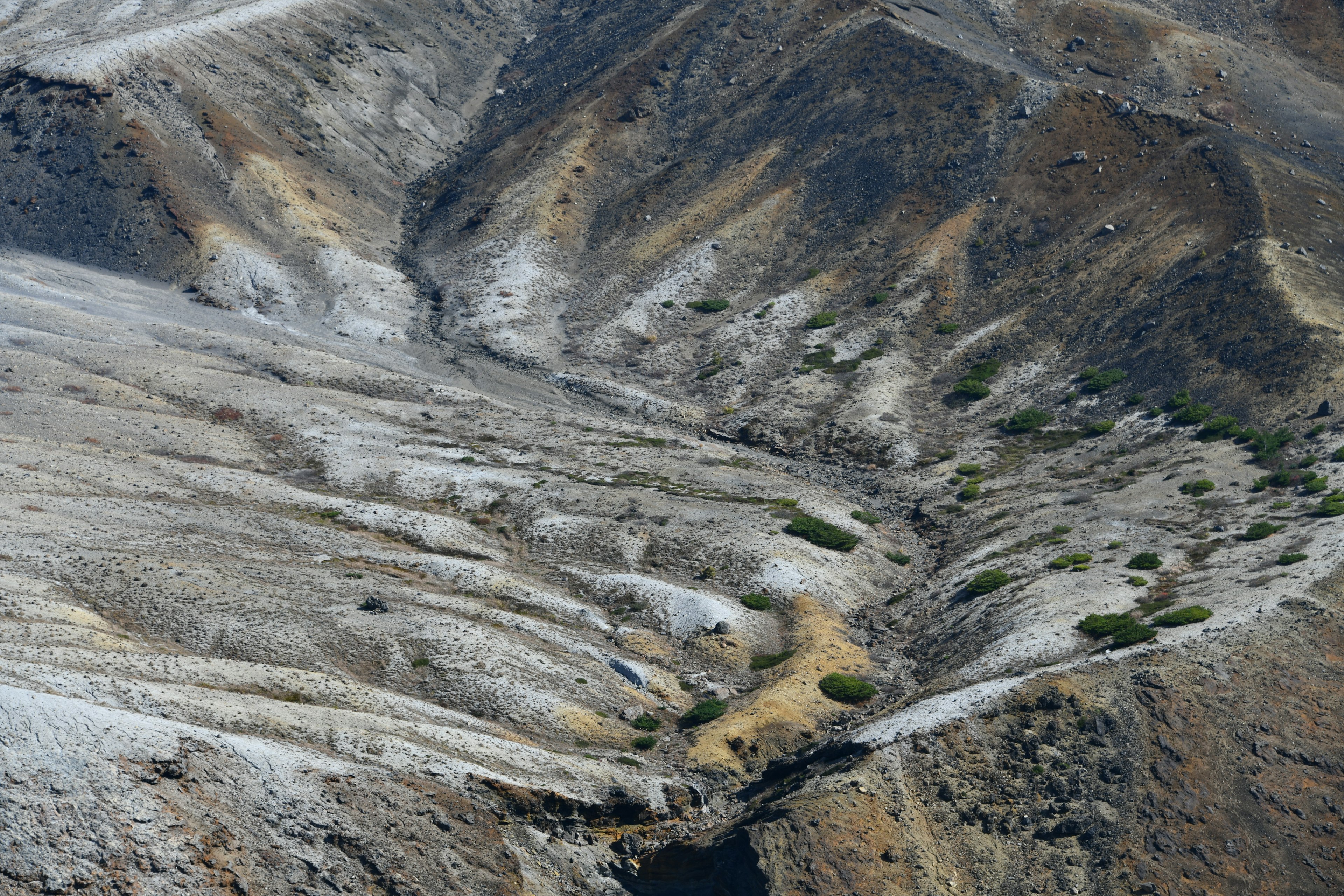 Vista aérea de laderas montañosas secas y un valle con vegetación verde escasa