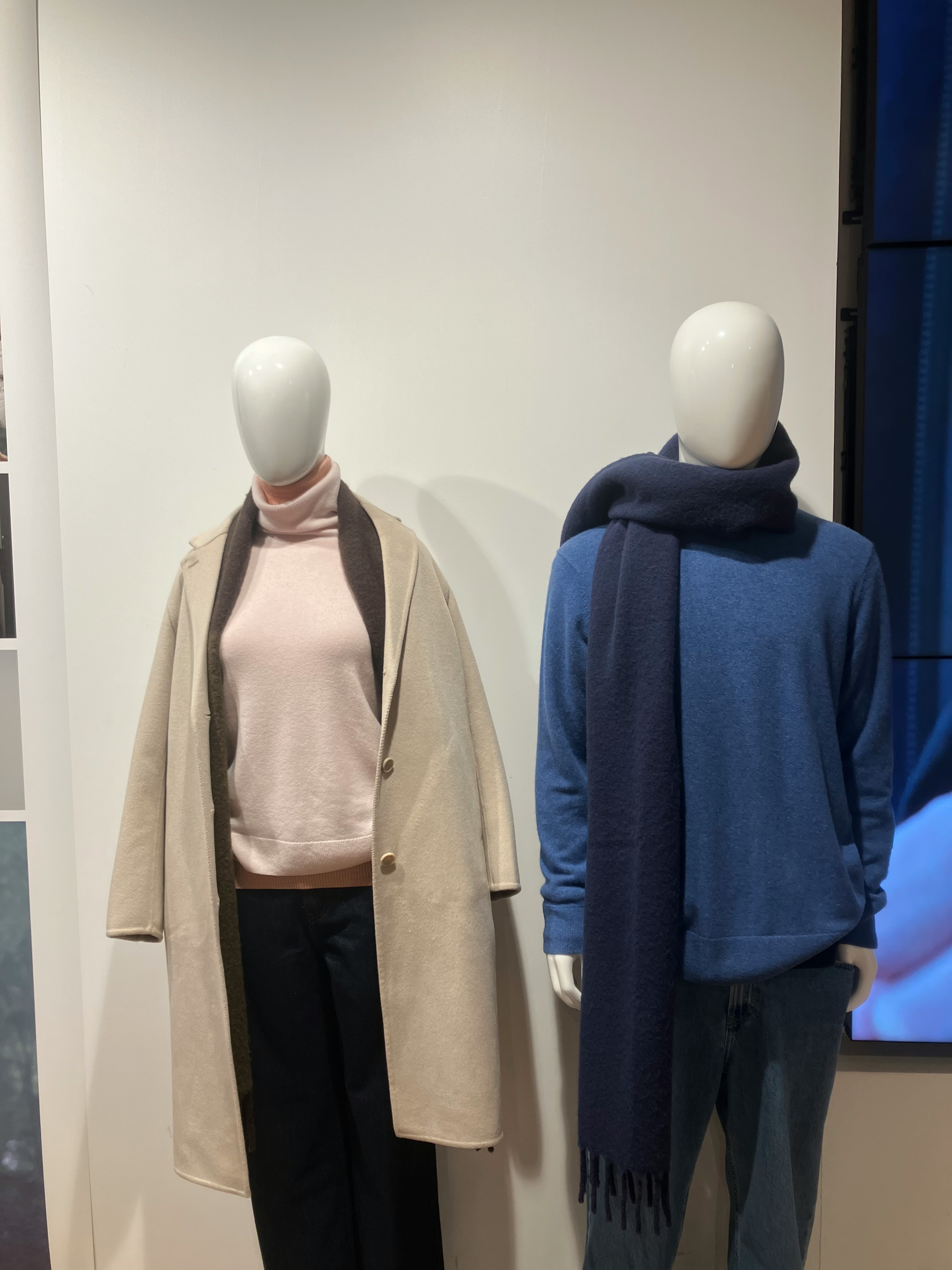 Affichage de mannequins dans un magasin de mode avec un manteau crème et un pull rose sur le mannequin de gauche et un pull bleu avec une écharpe marine sur le mannequin de droite