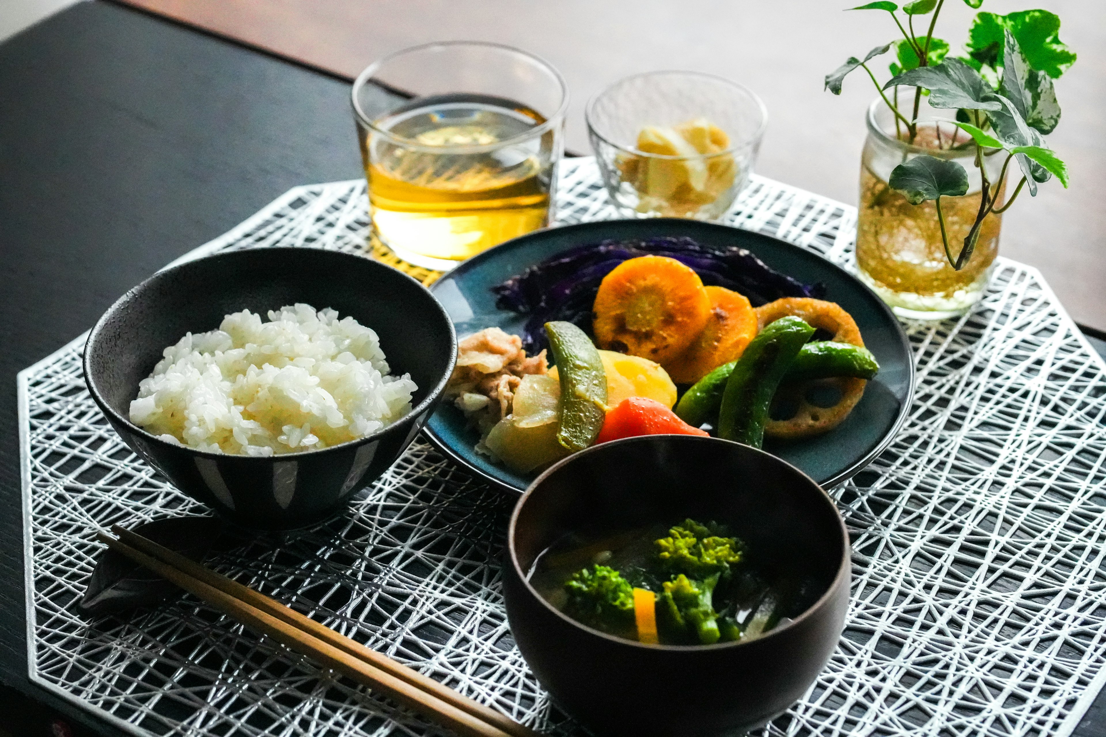 Japanese meal featuring rice, miso soup, assorted vegetables, and drinks