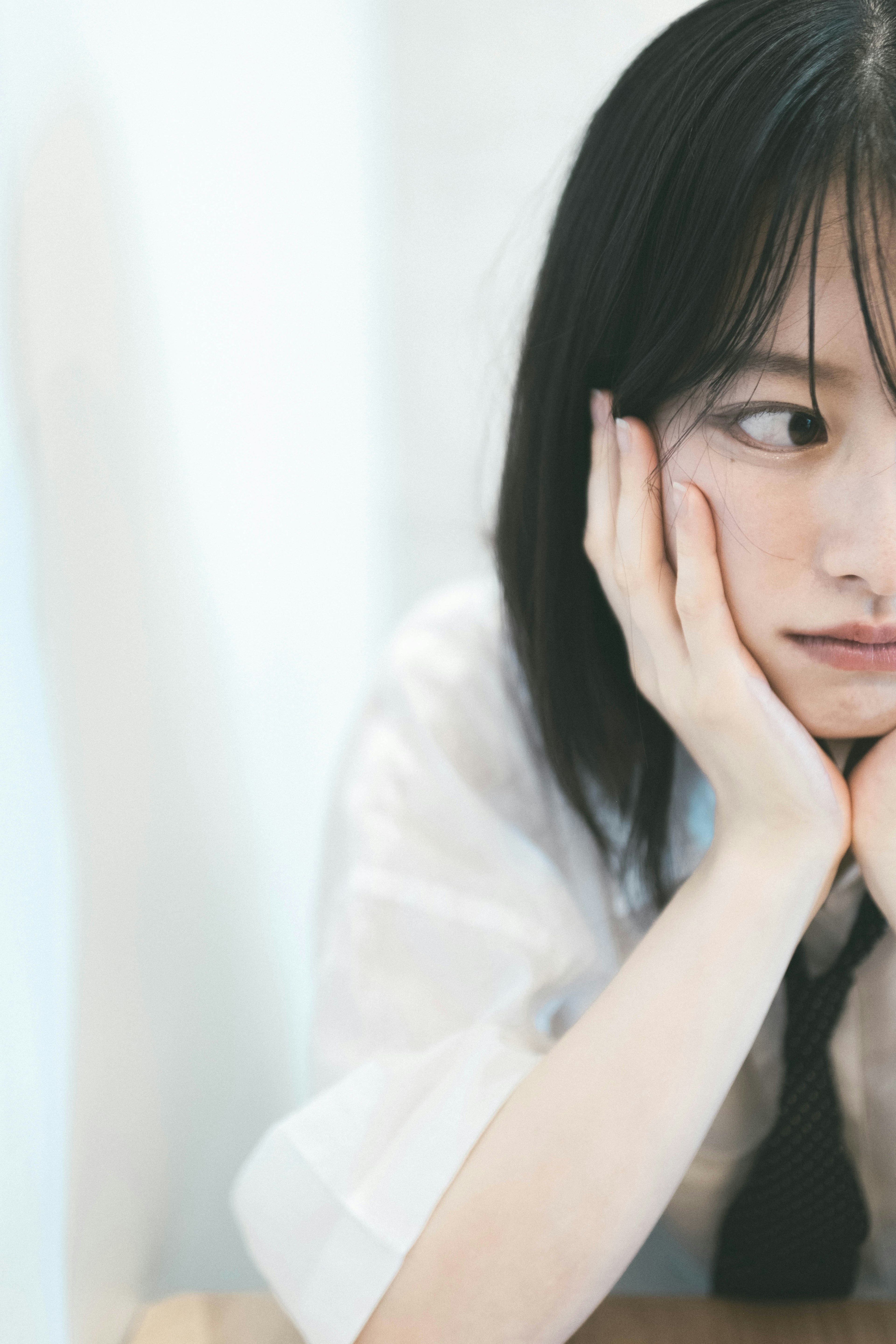 A young woman with a pensive expression resting her chin on her hand