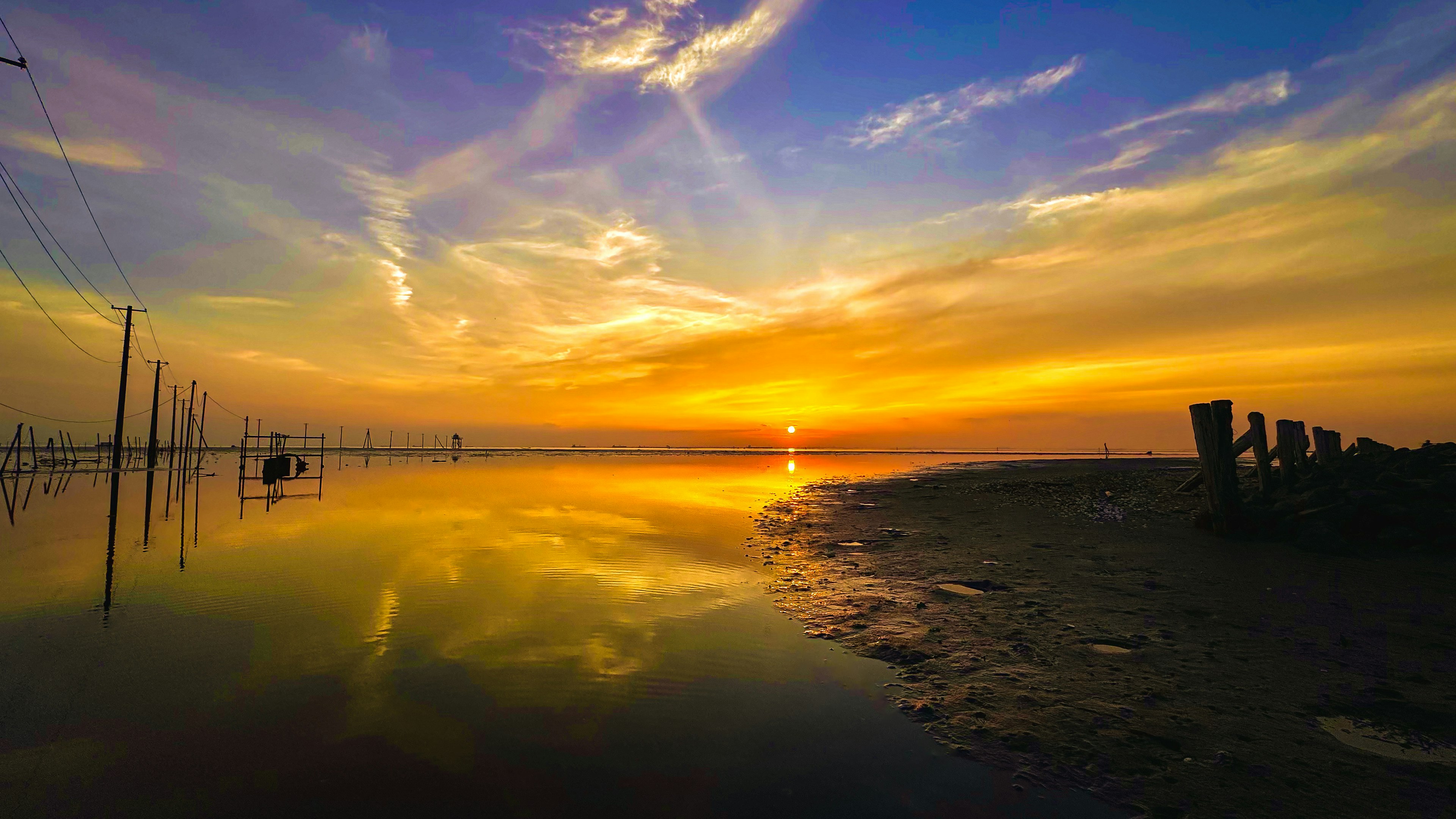 Hermoso paisaje de atardecer con cielo naranja y púrpura reflejado en la superficie de agua tranquila postes a lo lejos