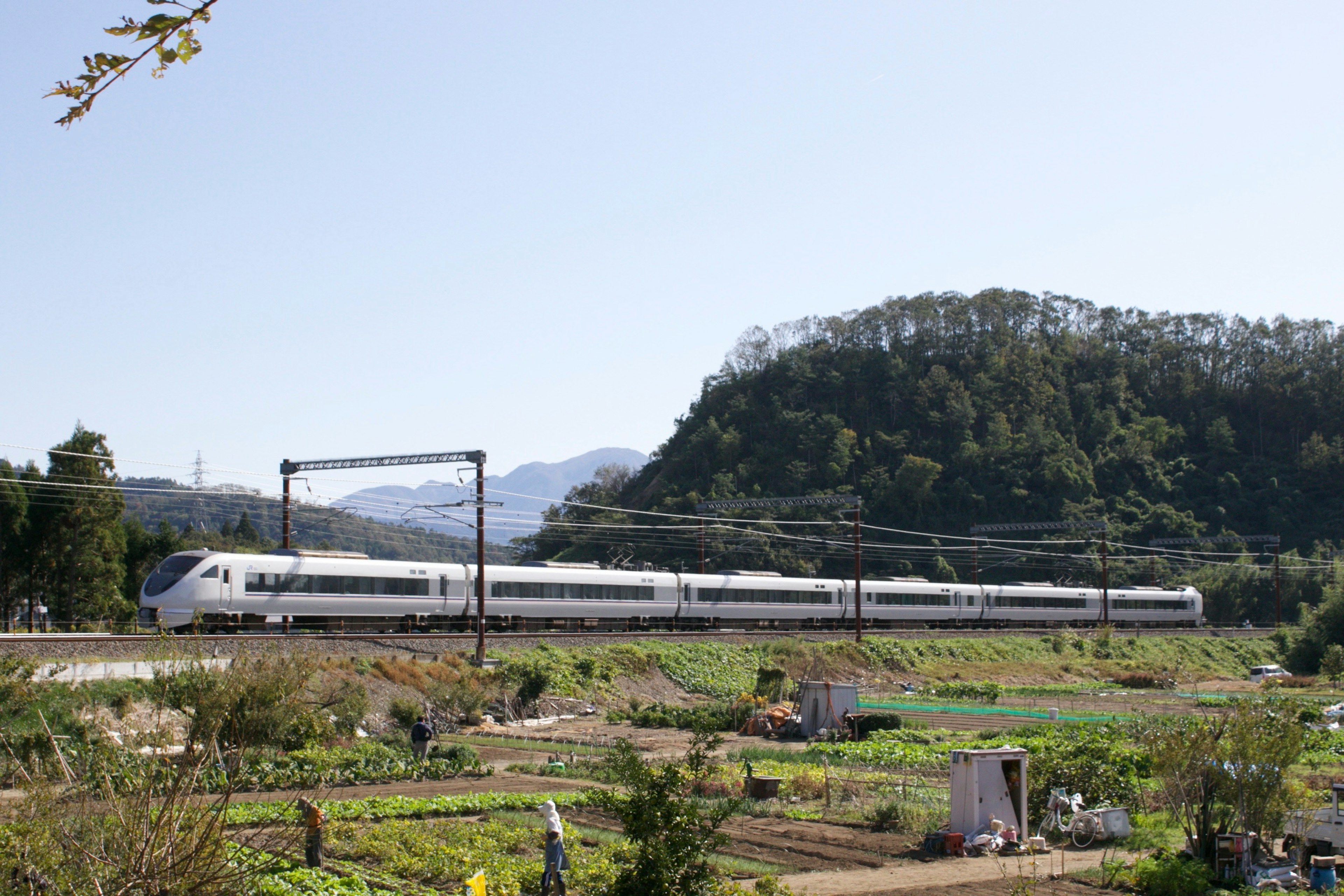 Shinkansen train running through rural landscape with mountains in the background