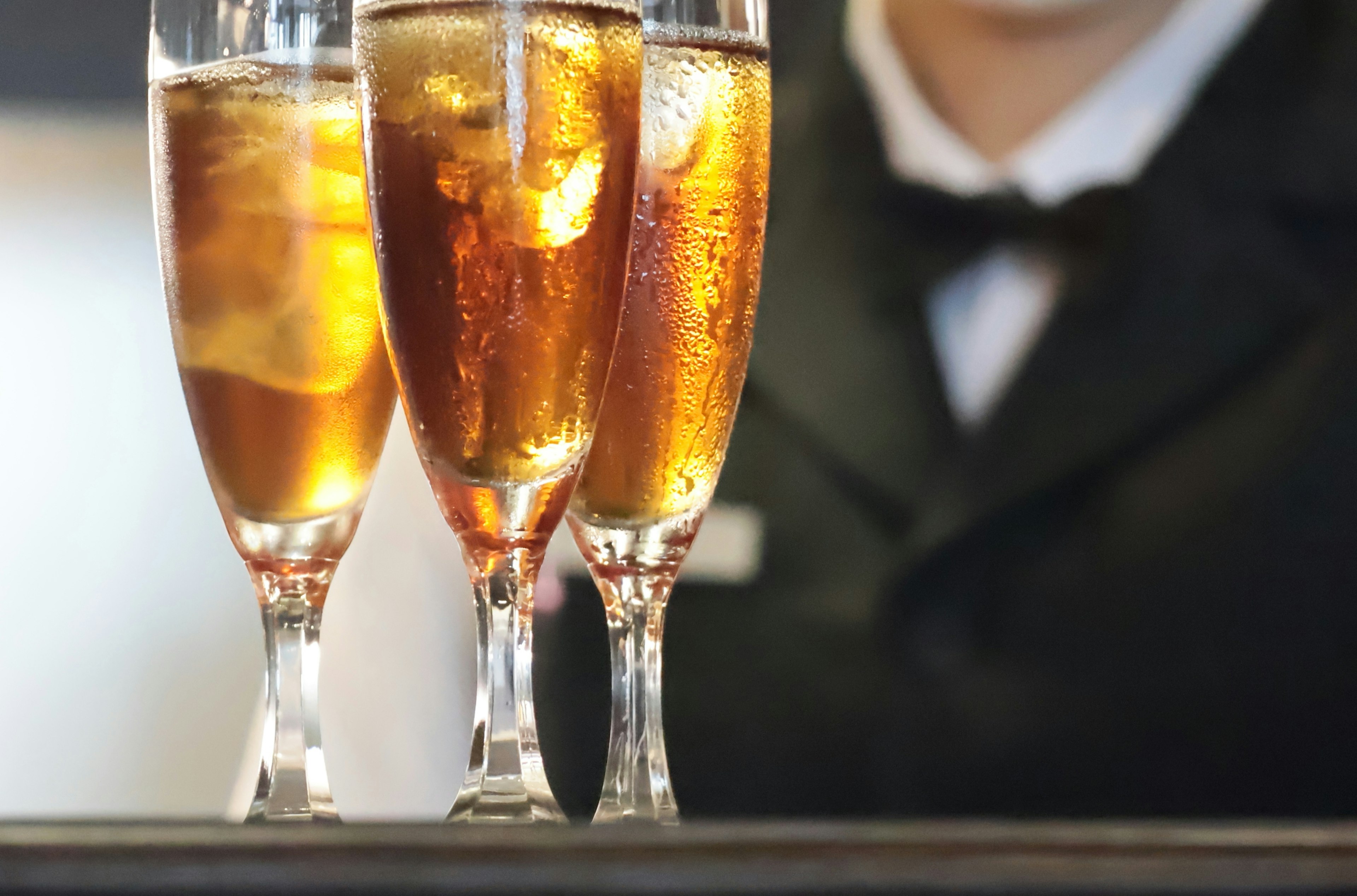 Three champagne glasses filled with sparkling drink and a staff member in a black suit