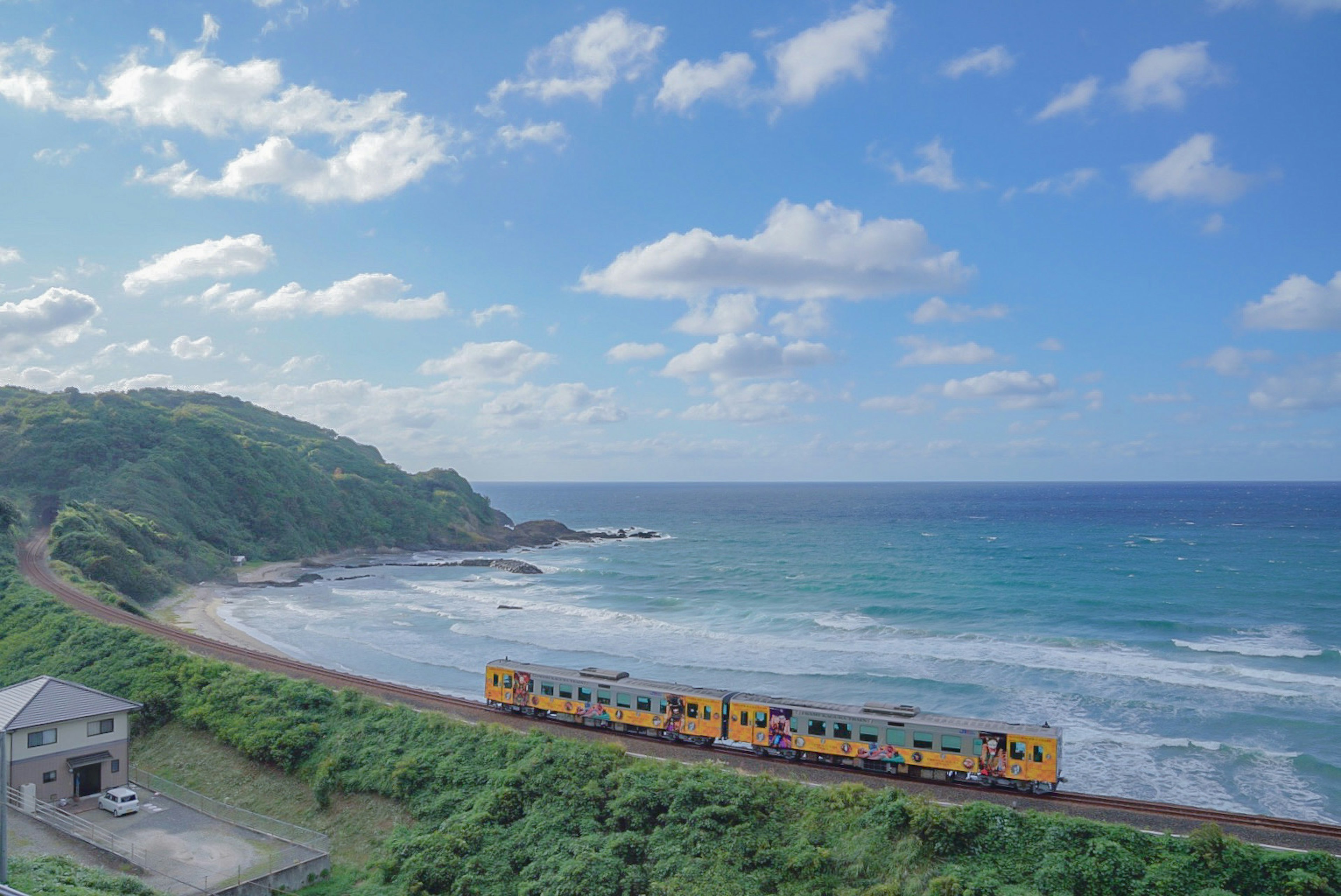 Tren amarillo corriendo por la costa con cielo azul