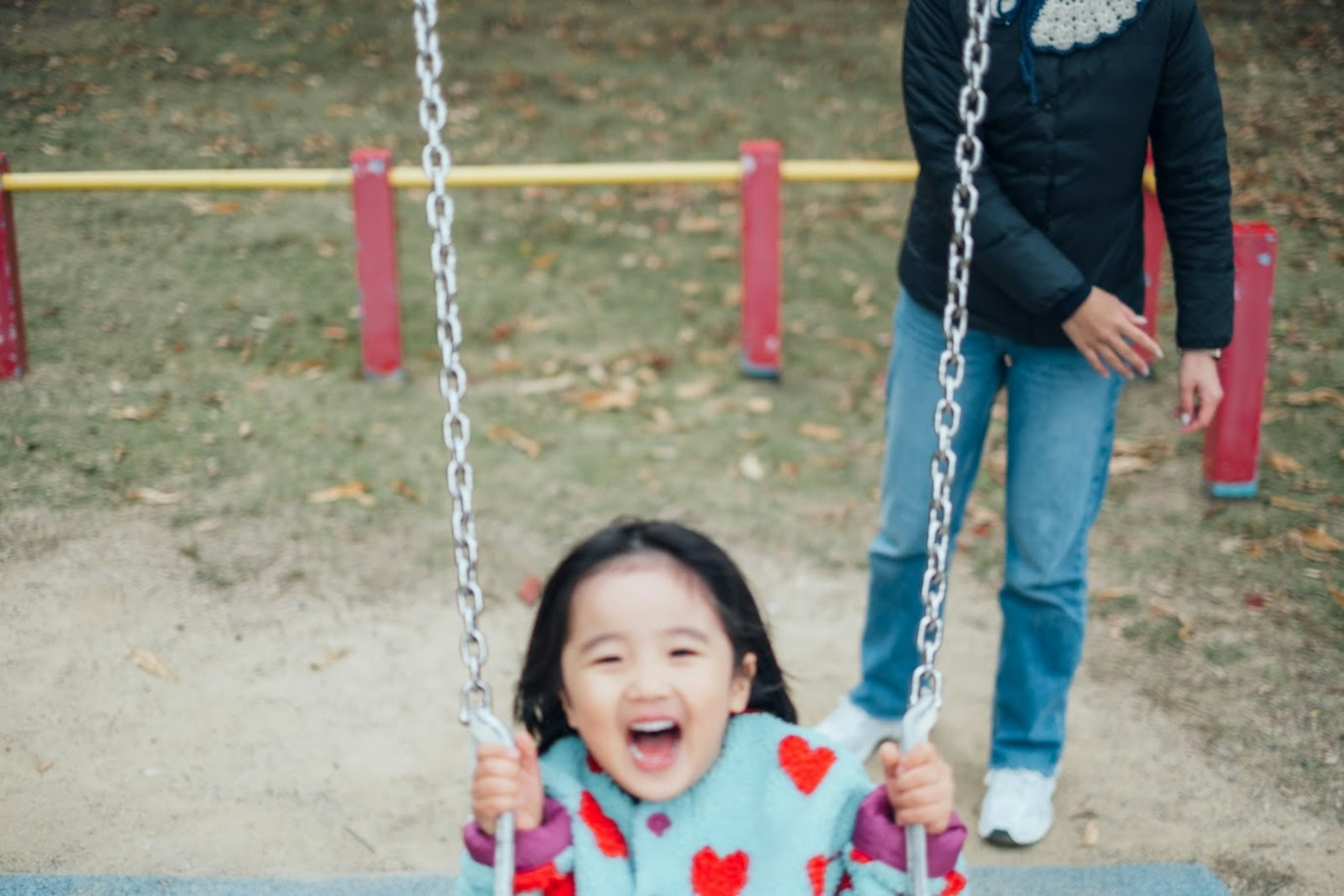 Bambina sorridente su un'altalena in un parco con un adulto sullo sfondo