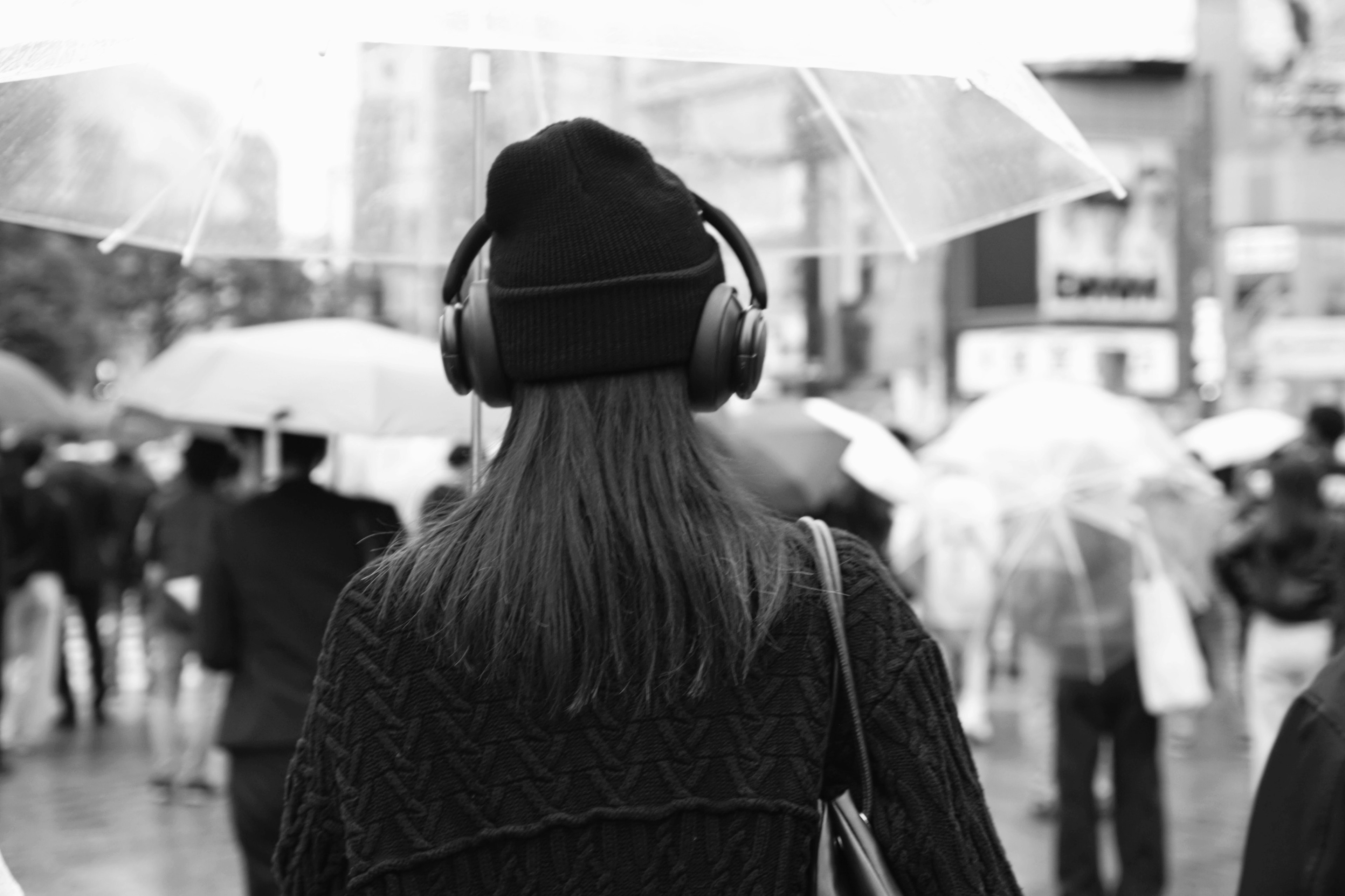 雨の中でヘッドフォンをつけた女性が後ろを向いているモノクロの風景