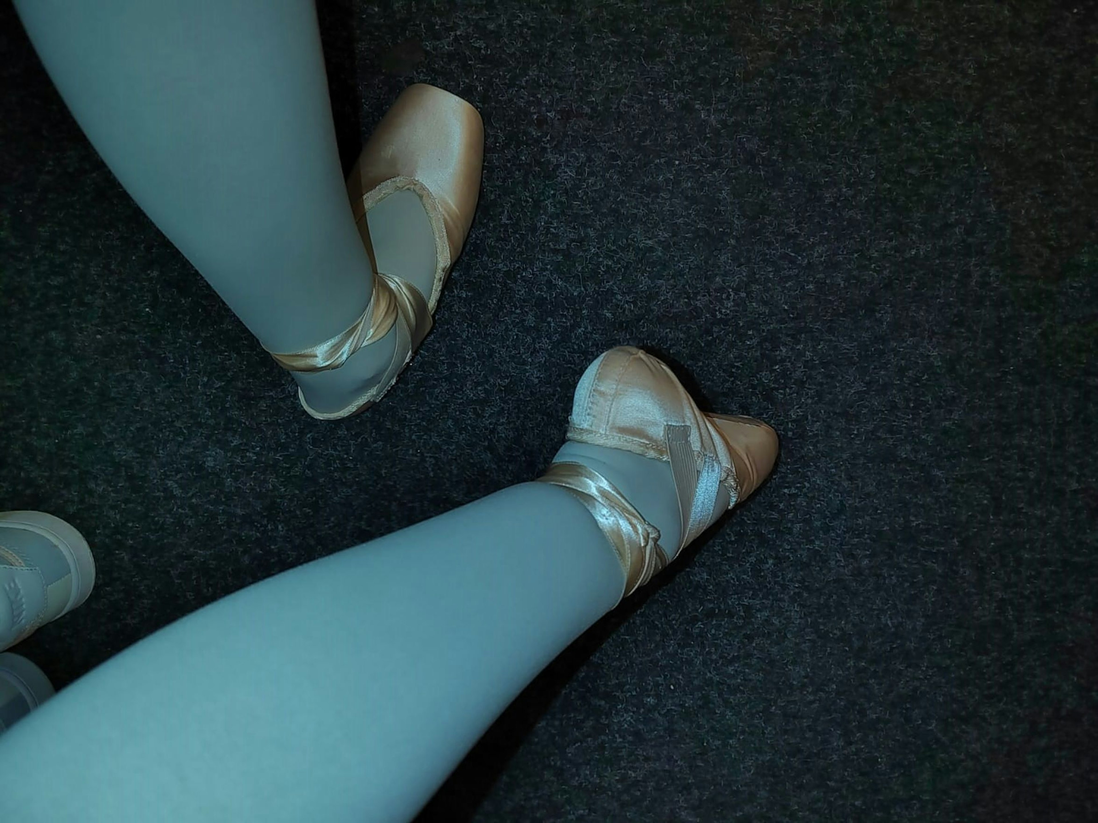 Close-up of ballet shoes worn with light blue tights on a dark floor