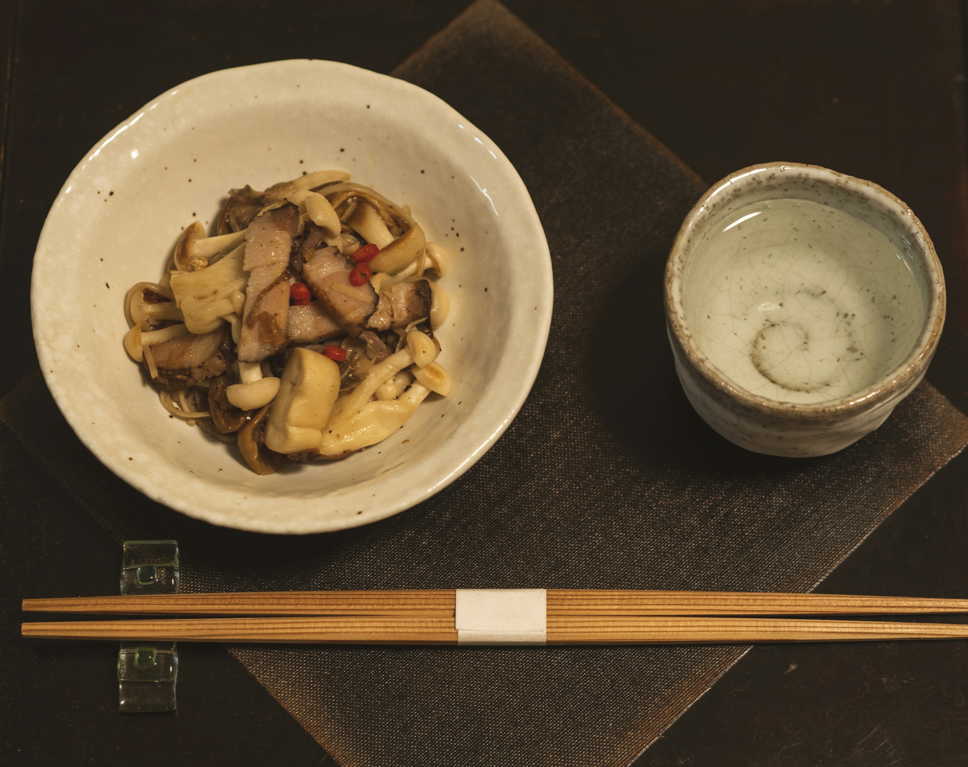 Plato de champiñones y carne en un tazón blanco junto a una pequeña taza de sake