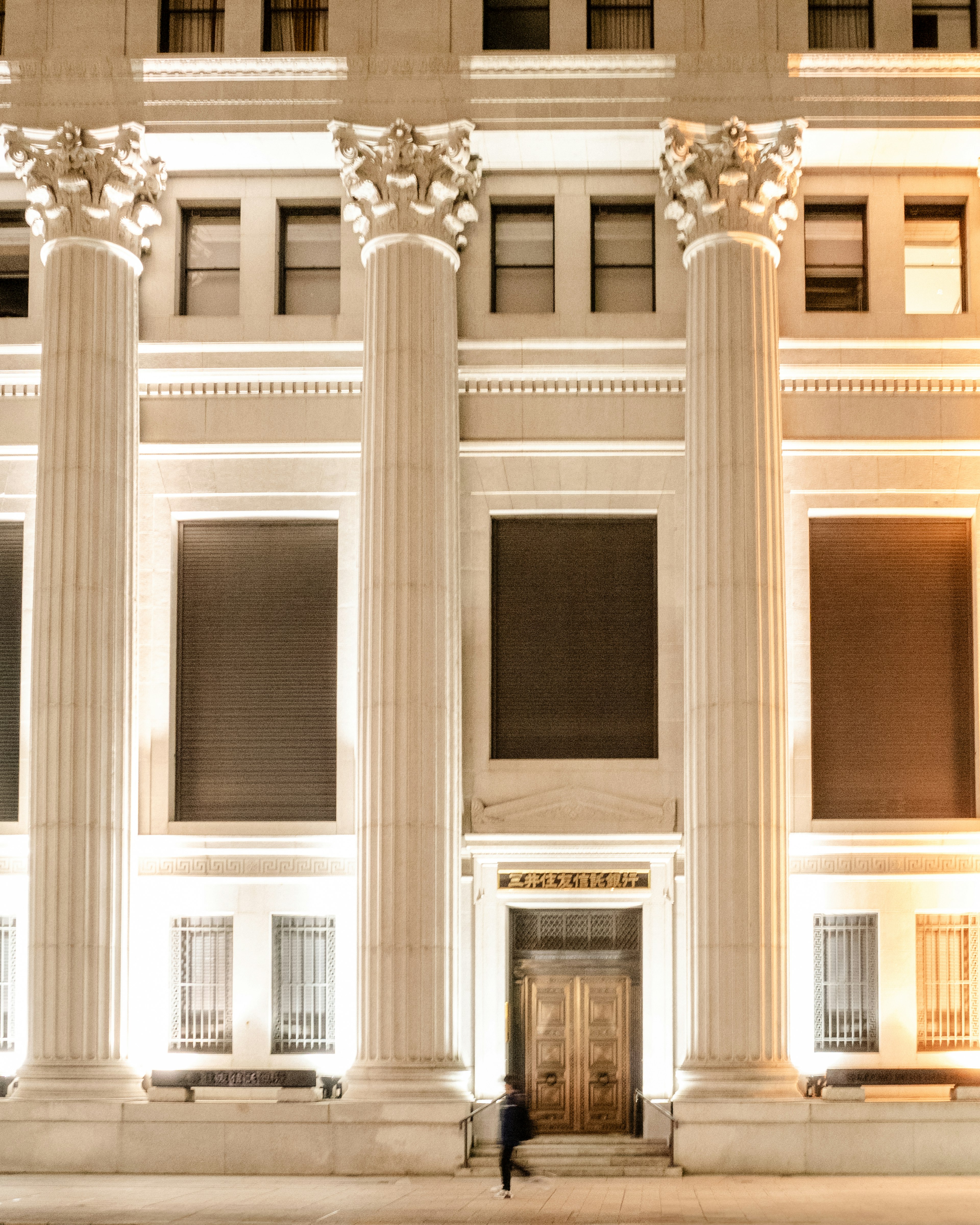 Una persona de pie frente a un gran edificio iluminado por la noche con columnas altas