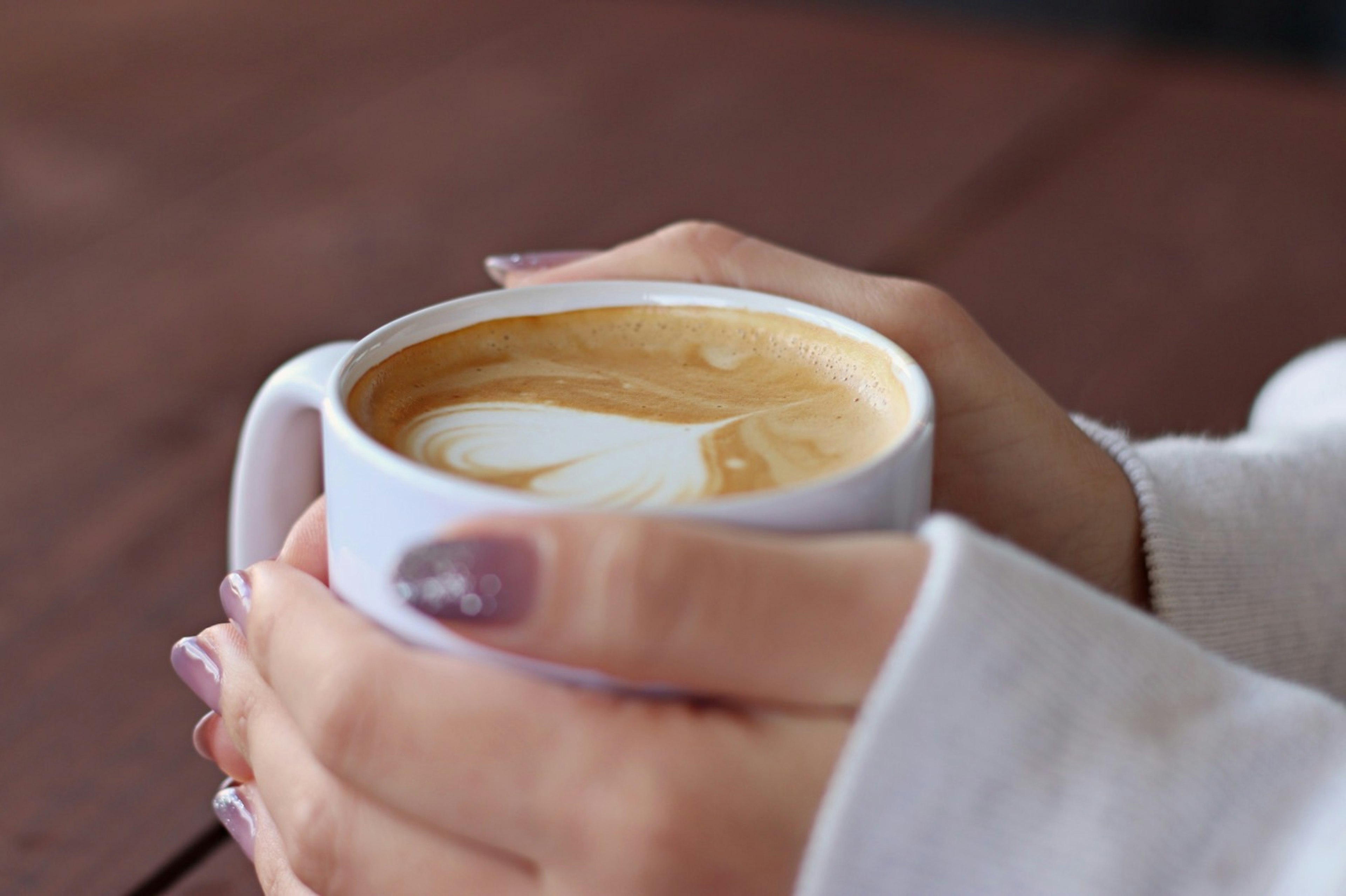 Hände, die eine Kaffeetasse mit einem herzförmigen Sahnemuster halten