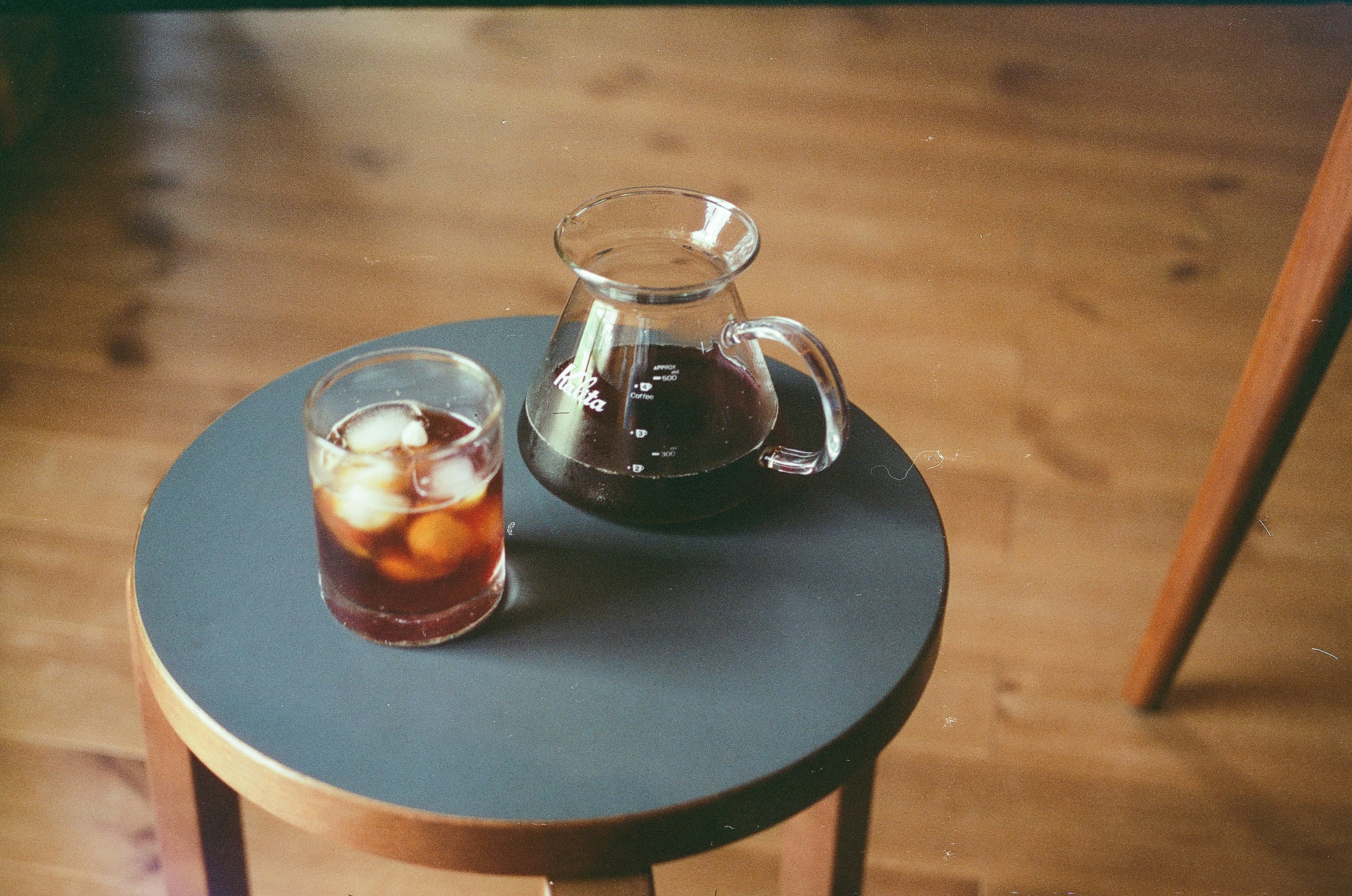 Un bicchiere di caffè freddo e una caraffa su un tavolo con pavimento in legno