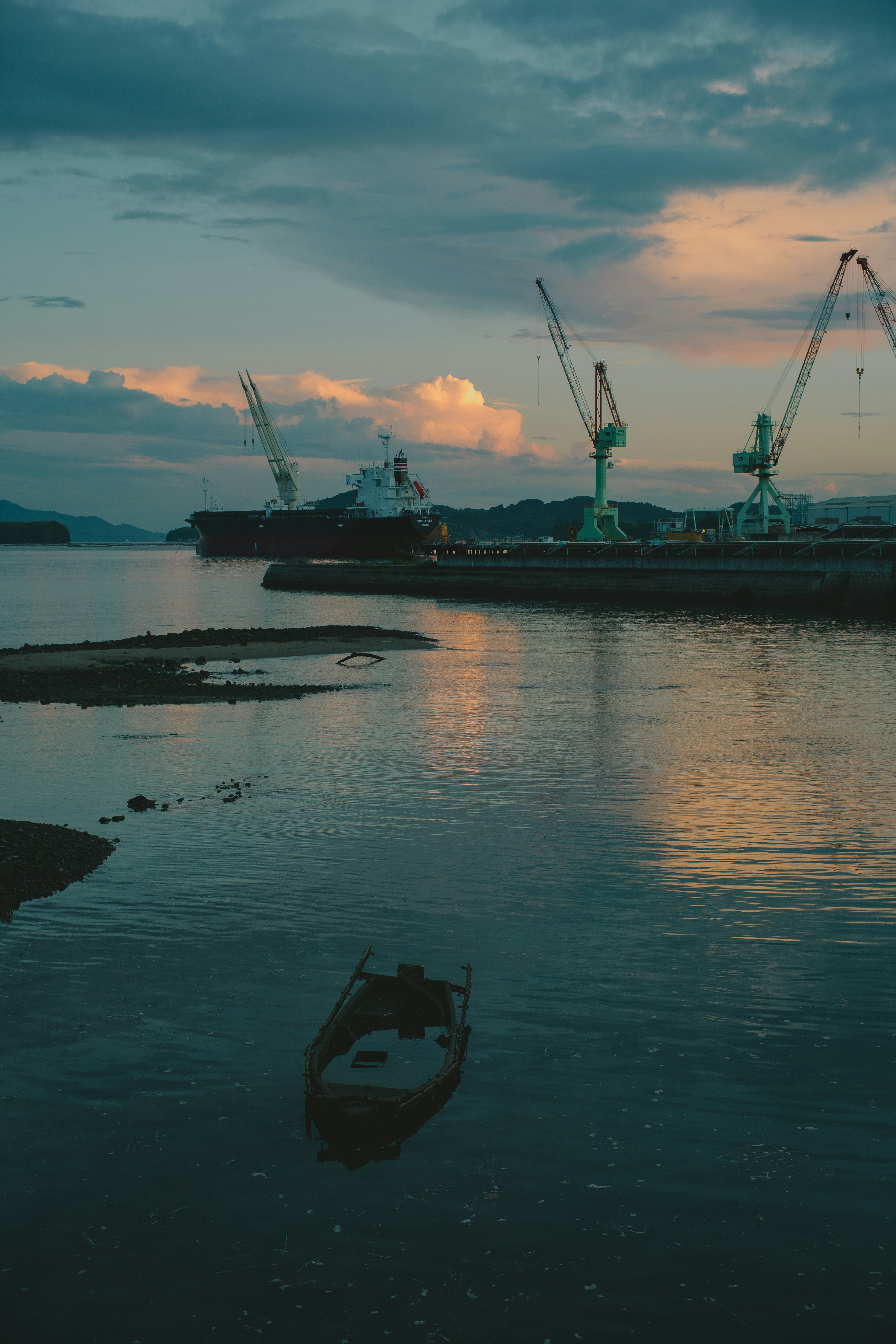 Scène de port calme avec des grues et des bateaux reflétés sur l'eau au coucher du soleil