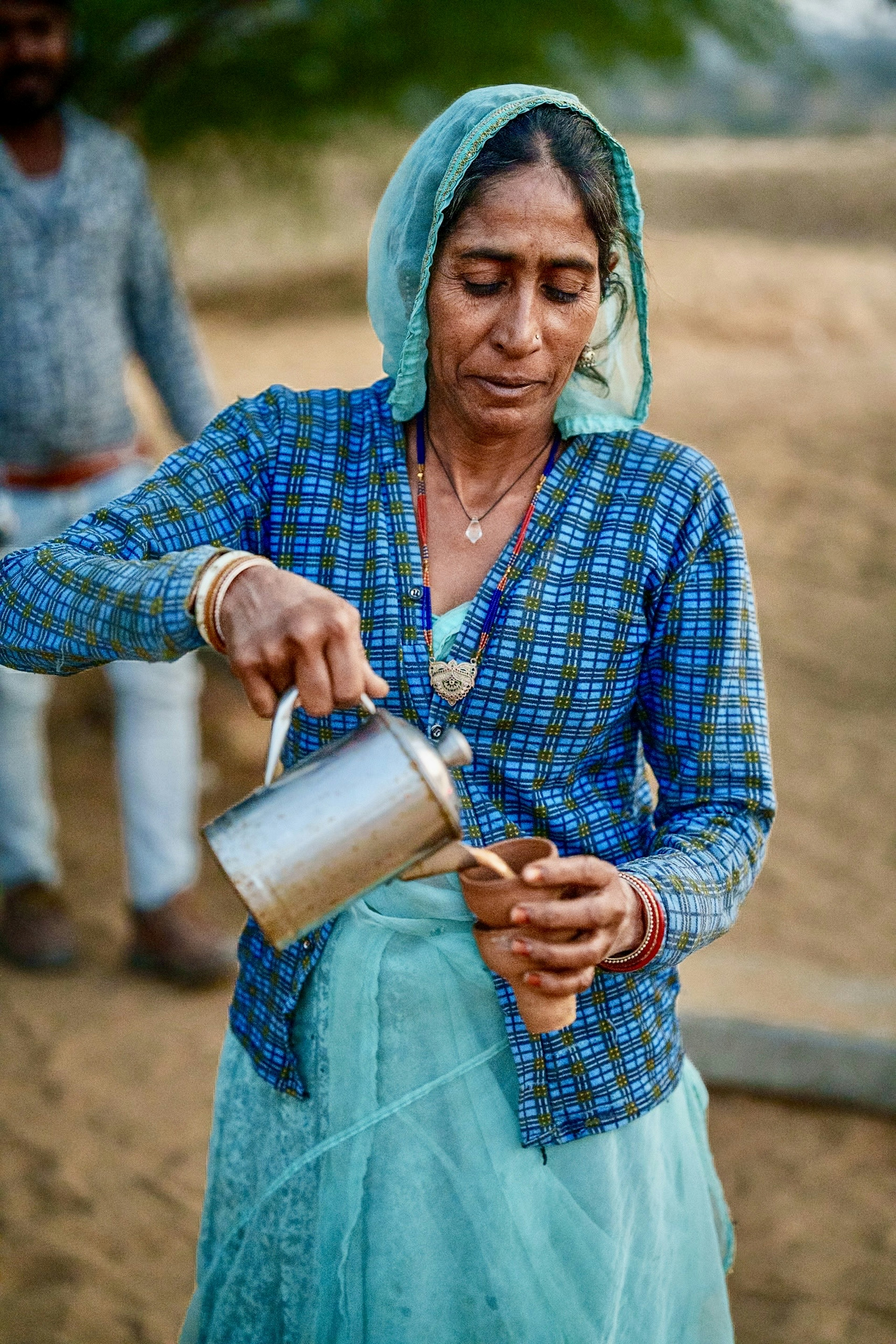 Femme versant de l'eau portant une chemise à carreaux bleue et un foulard