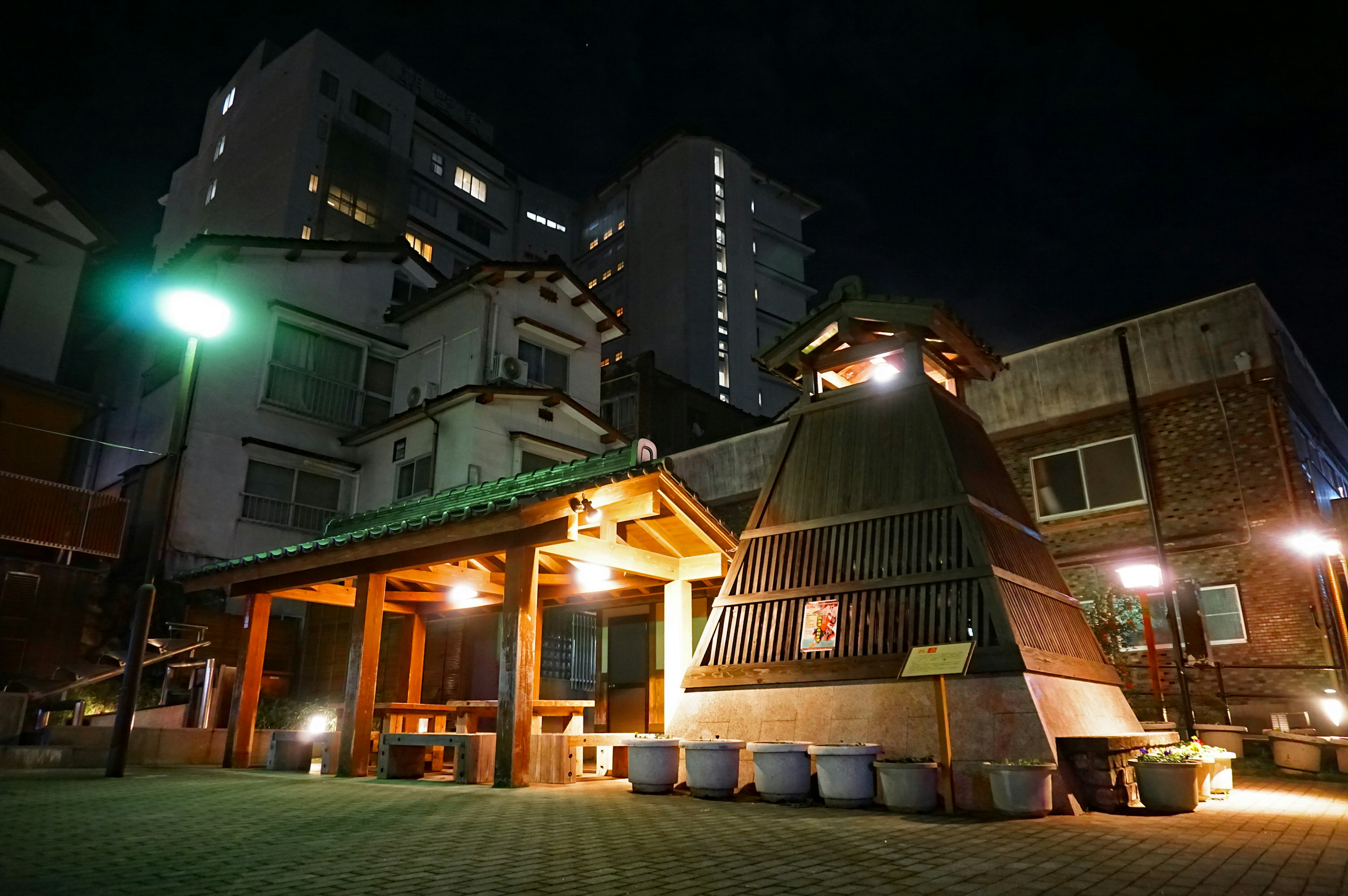 Bâtiment traditionnel d'onsen illuminé la nuit entouré de bâtiments modernes