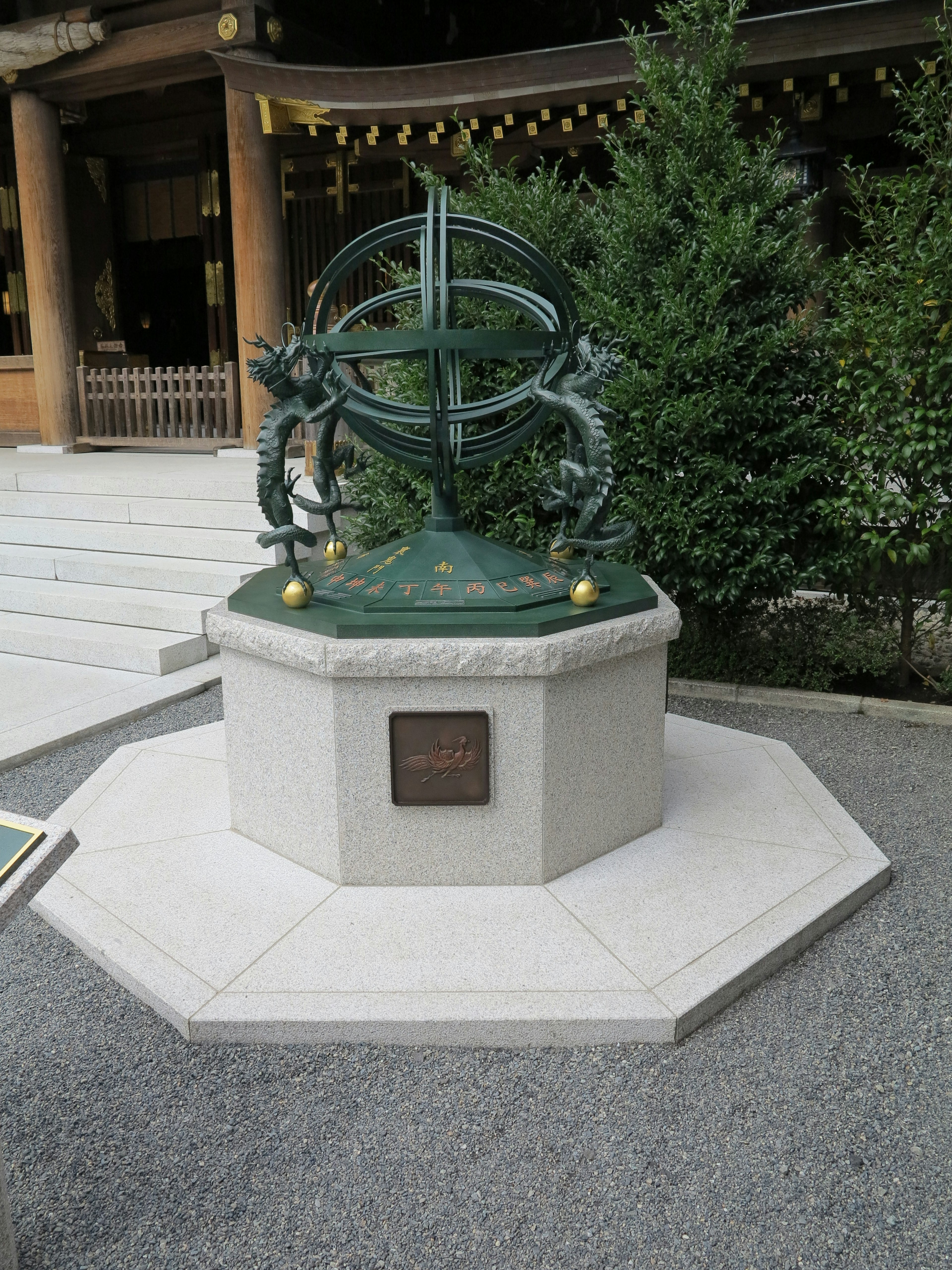 Bronze armillary sphere on an octagonal pedestal surrounded by greenery