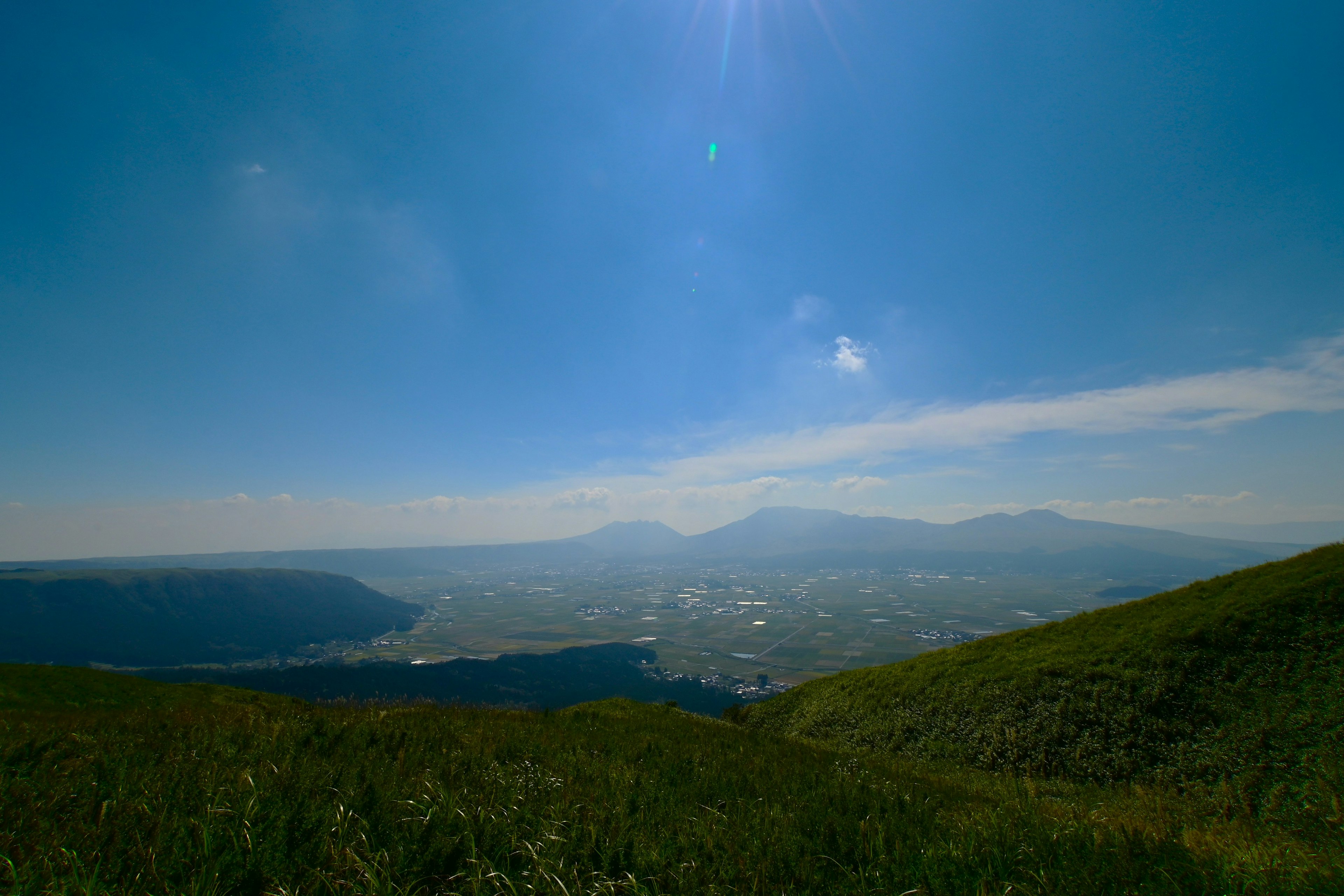 Bukit hijau luas di bawah langit biru dengan gunung jauh