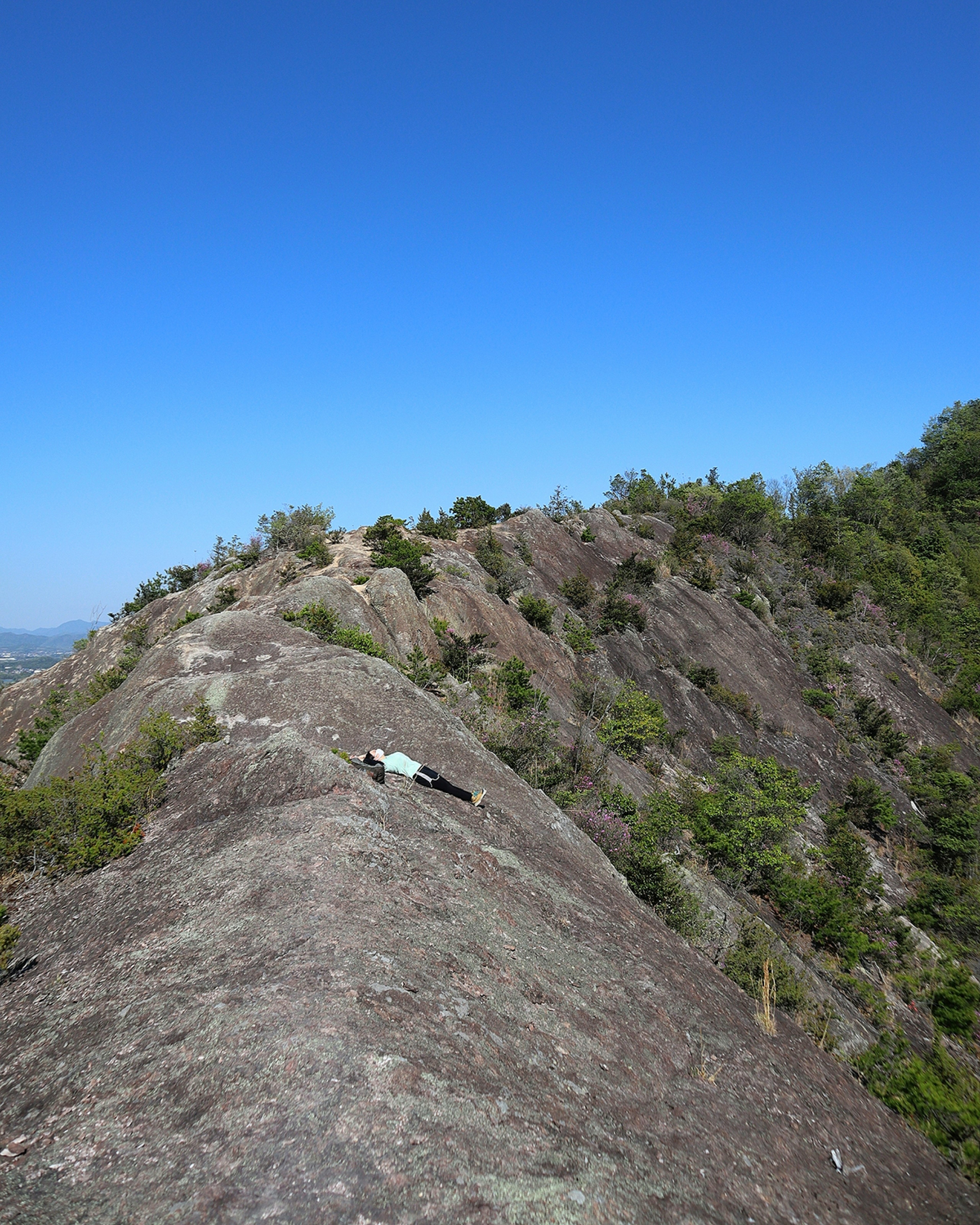 Hiker lying on a rocky ridge under a blue sky