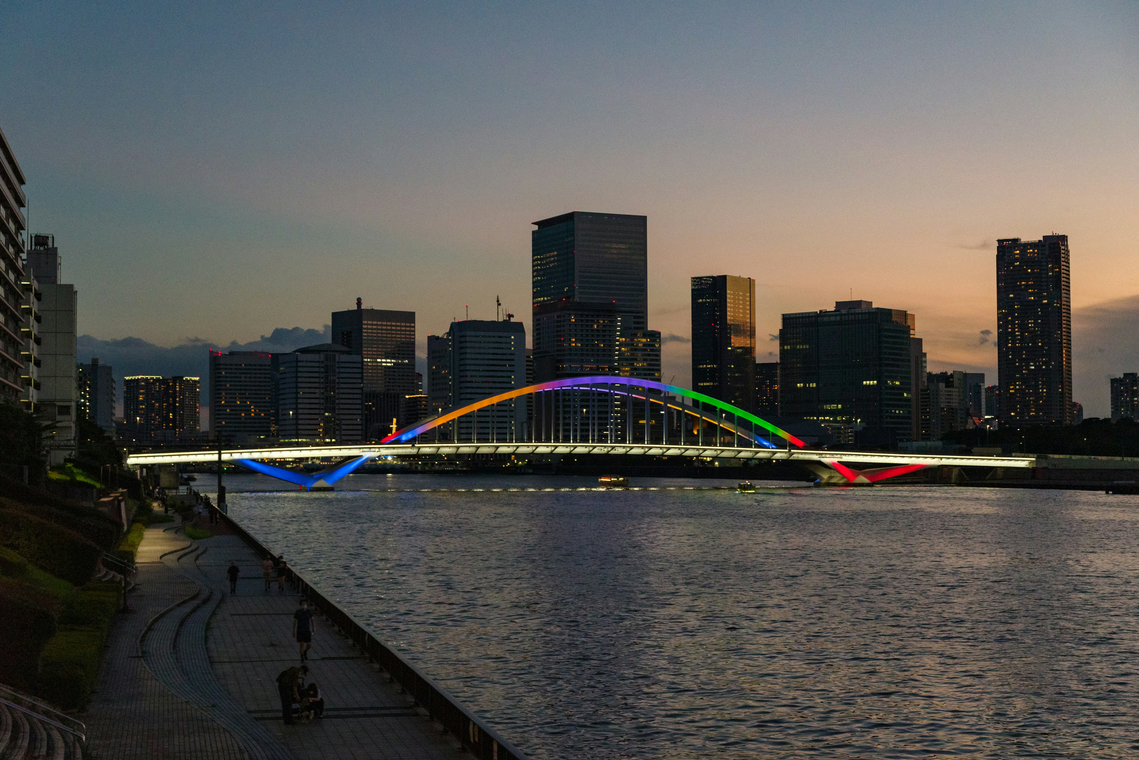 Puente arco iris iluminado al atardecer con el horizonte de Tokio al fondo