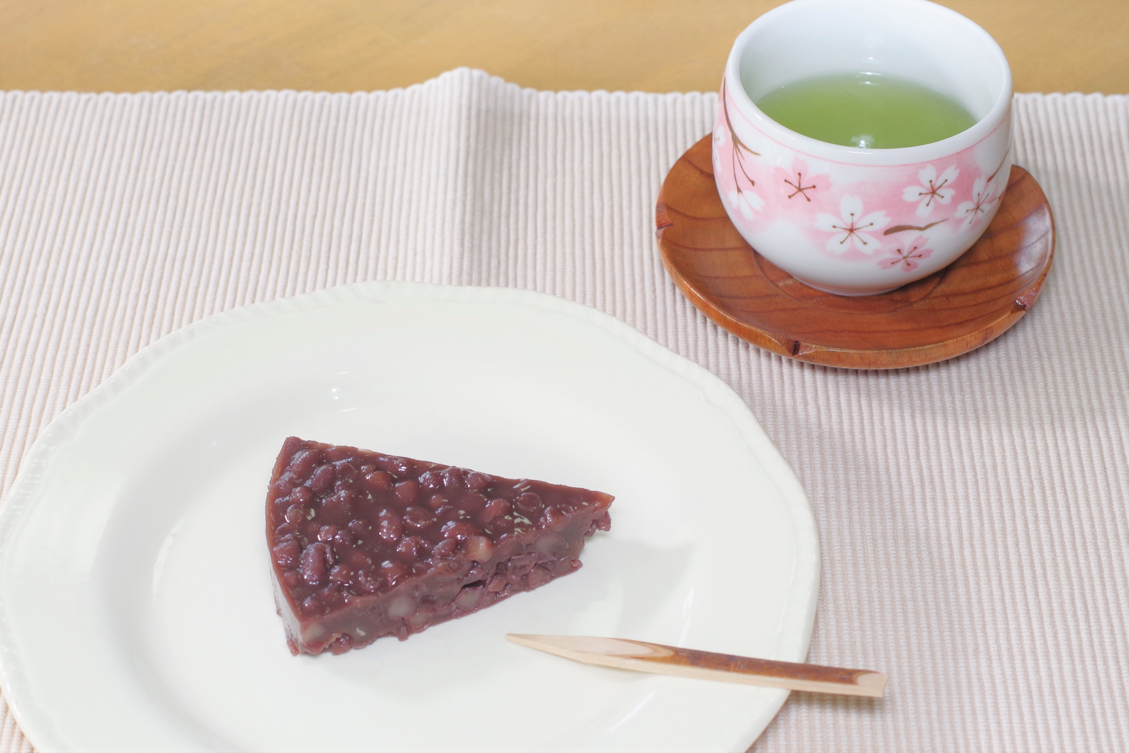 A set of wagashi and green tea featuring anko cake on a white plate with a sakura patterned teacup