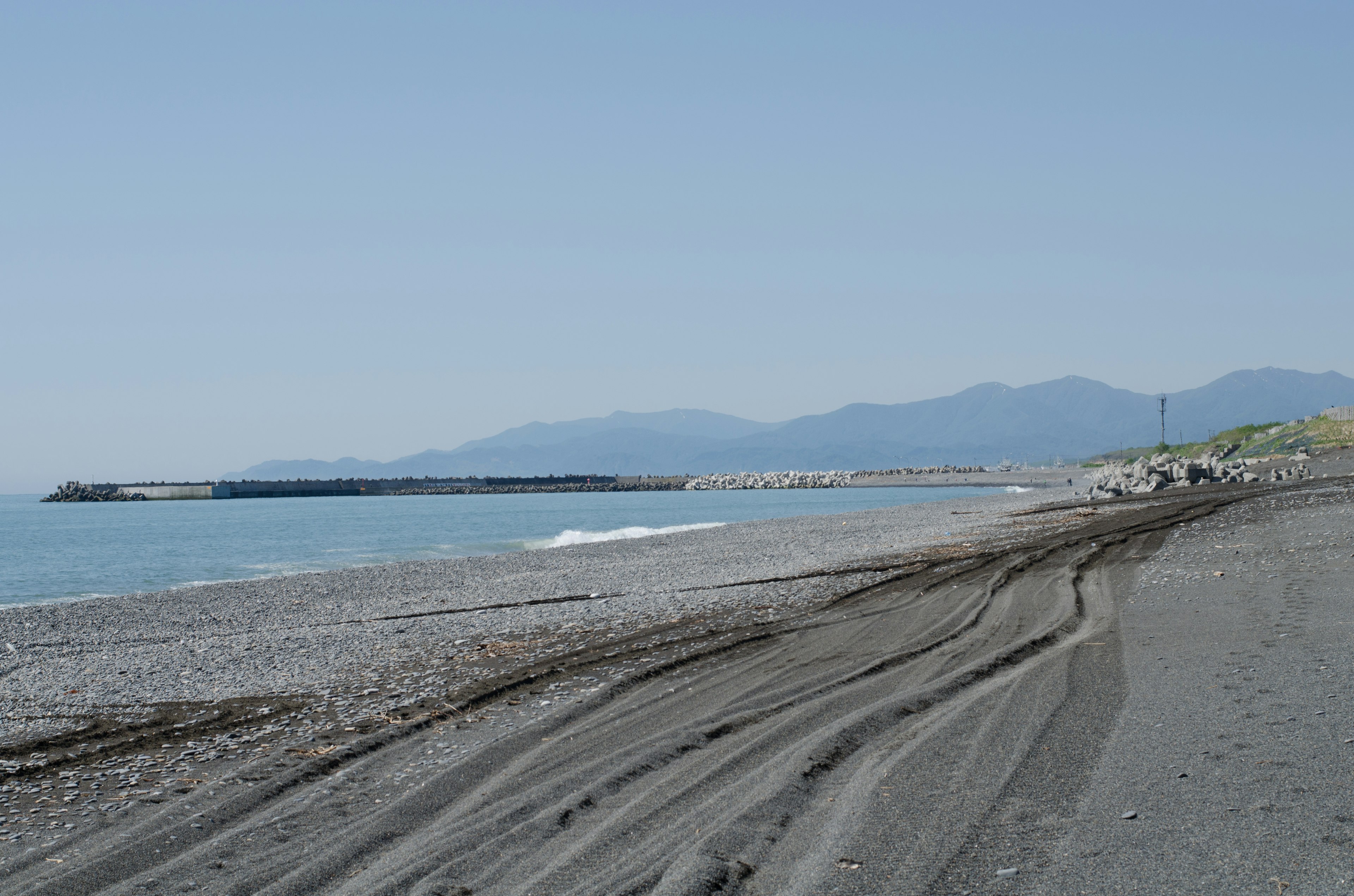 Scena di spiaggia serena con sabbia nera e mare calmo, montagne in lontananza