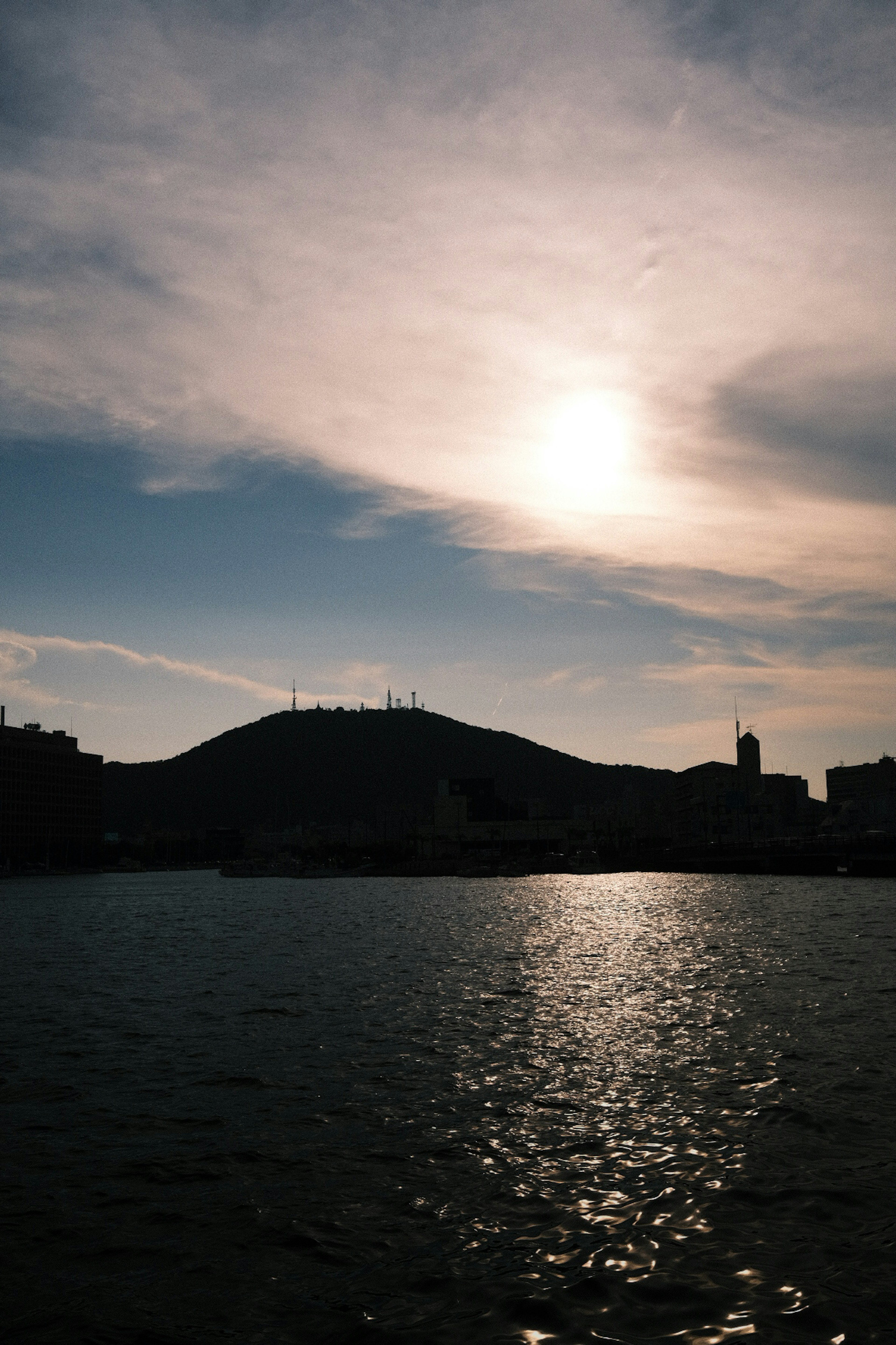 Vista en silueta de colinas con reflejo del sol en el agua y cielo nublado