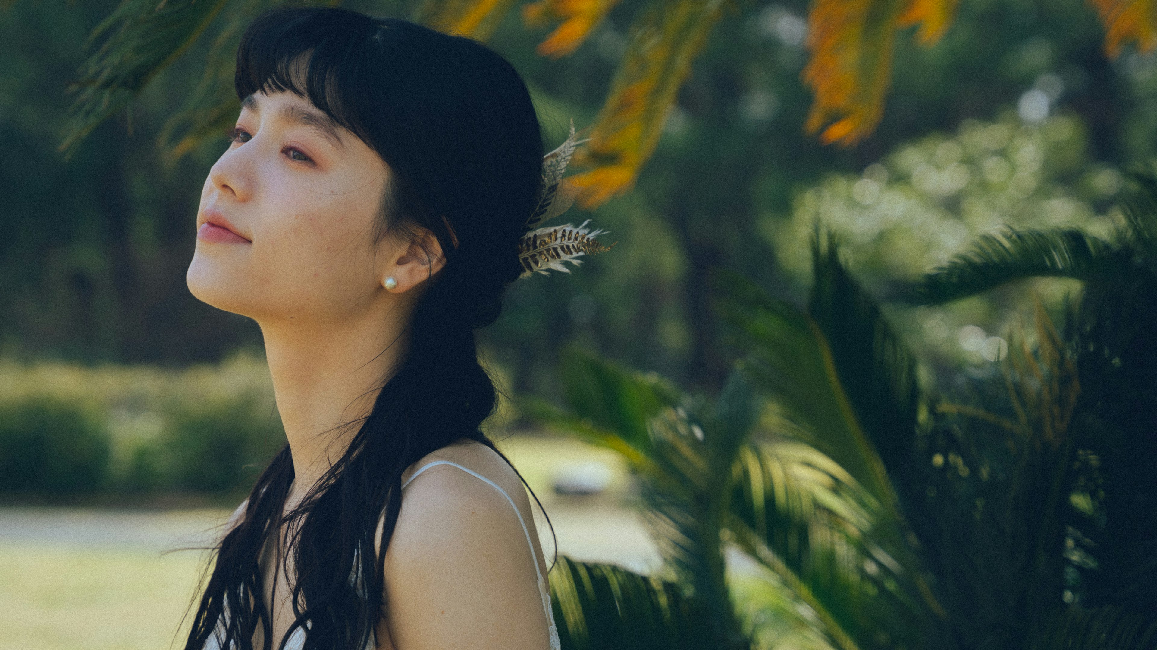 Profil d'une femme souriante dans la nature avec un accessoire floral dans les cheveux et un fond vert