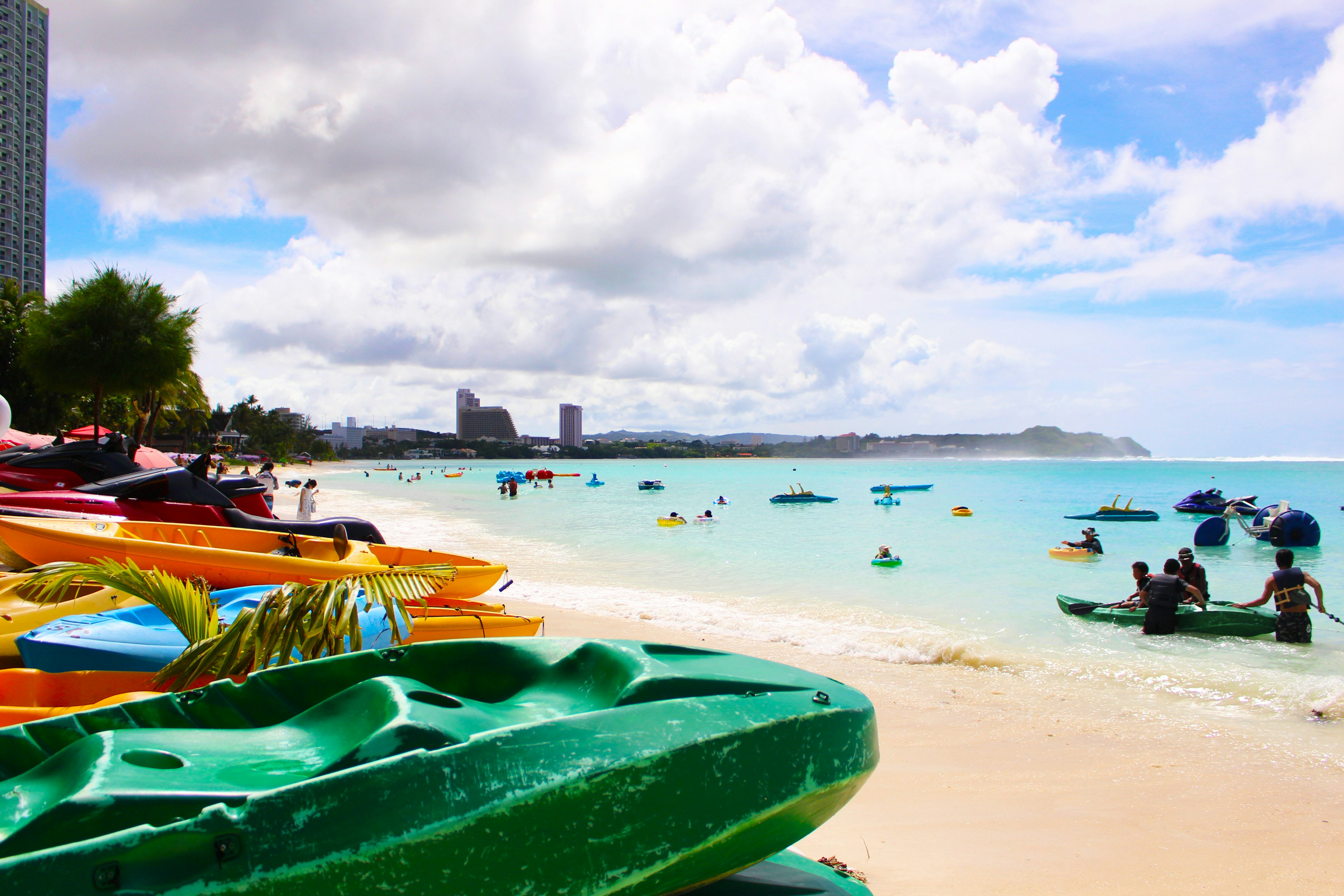 Kayaks lined up on the beach with people enjoying the blue sea