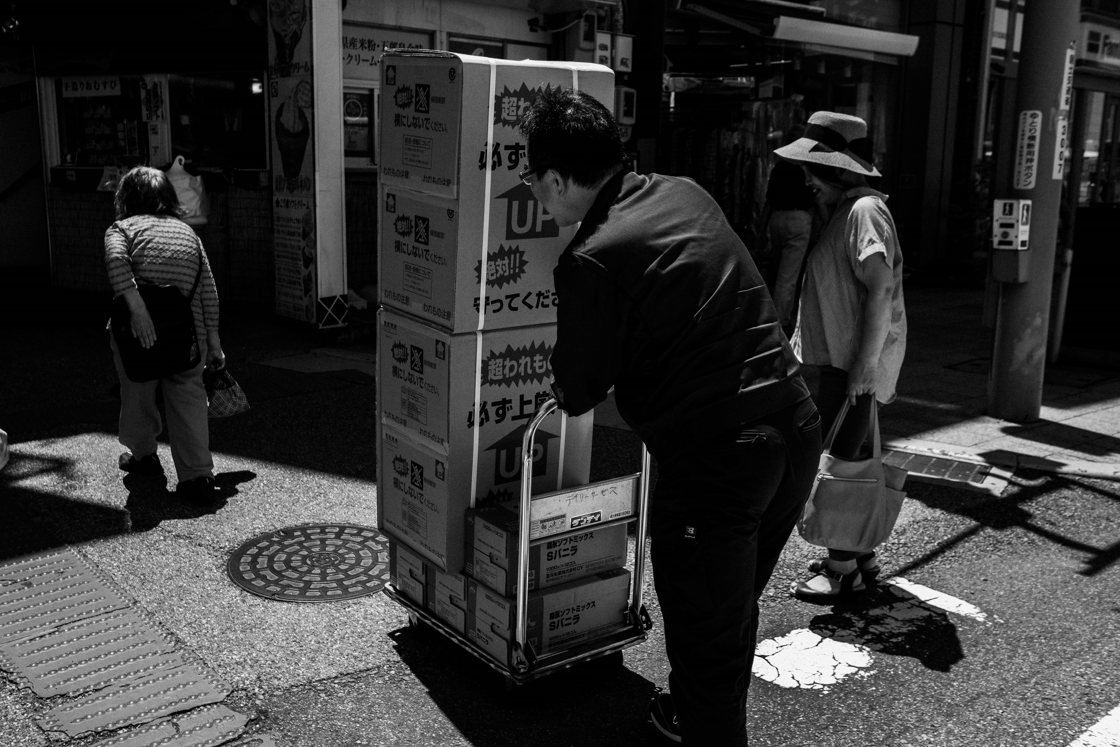 Man pushing a cart of boxes on a busy street with pedestrians