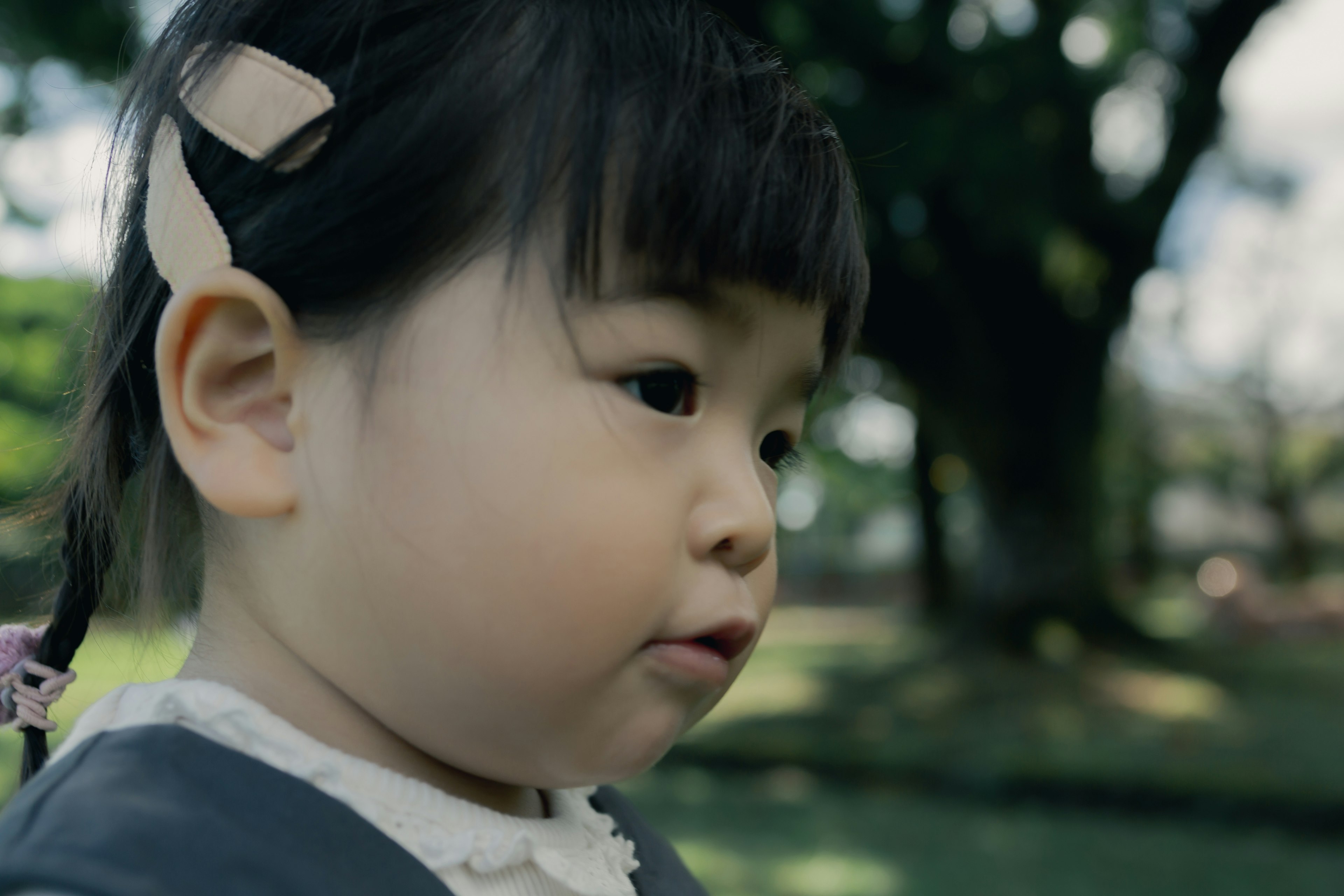 Perfil lateral de una niña pequeña jugando en un parque con cabello negro y una cinta sobre un fondo verde