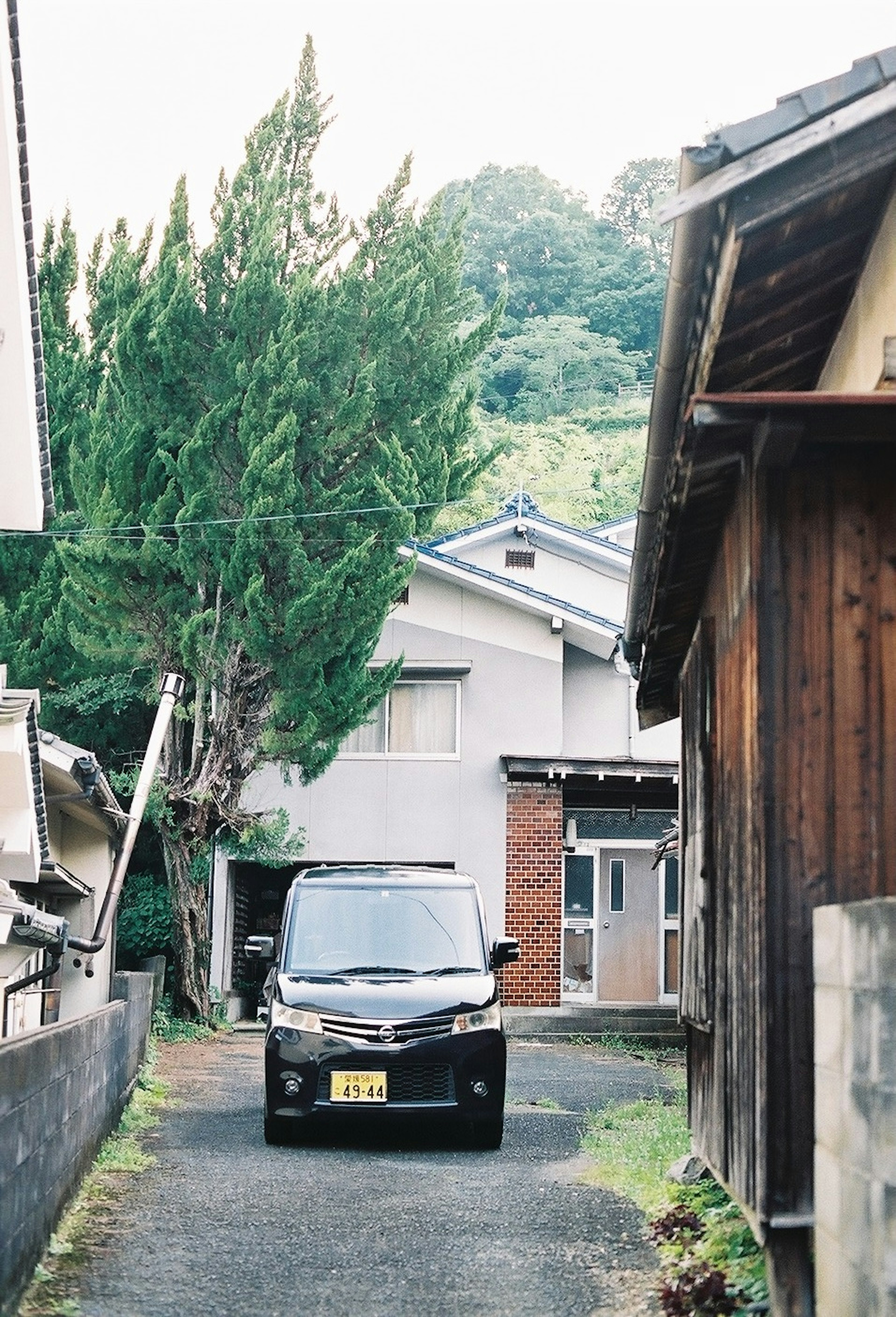 A narrow path with a parked black car and surrounding houses