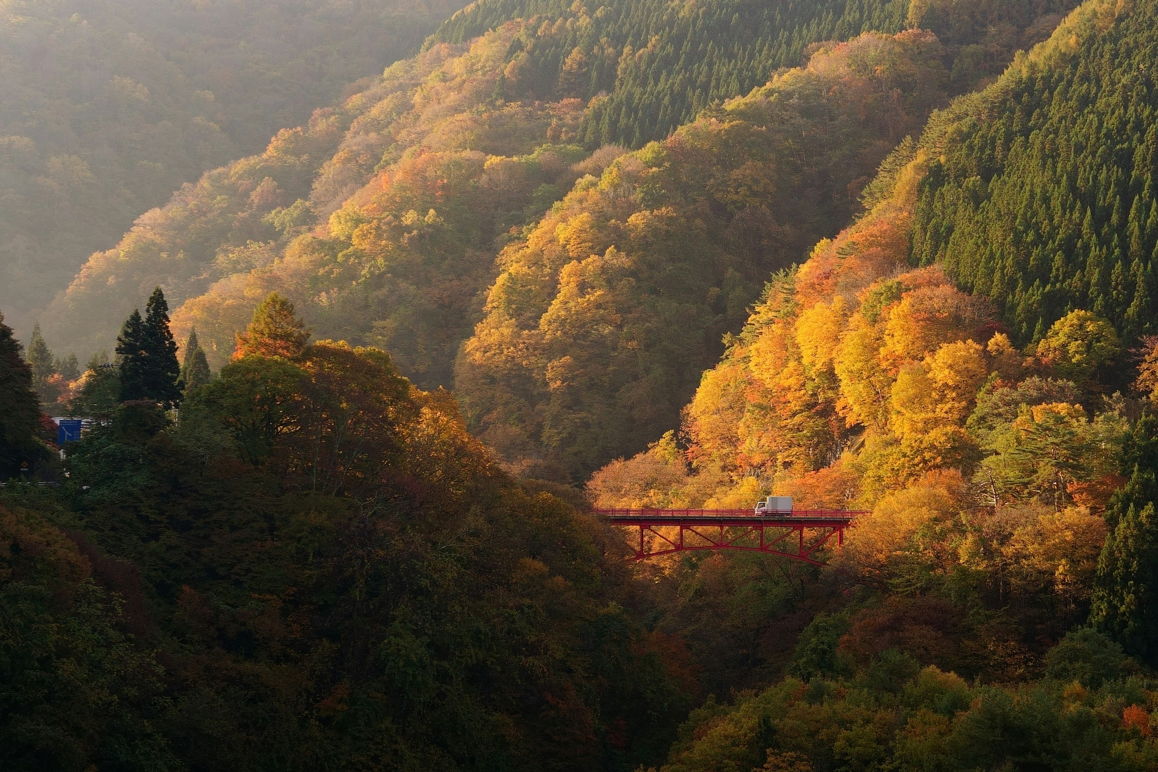 Autumn foliage covering mountains and valley with a bridge