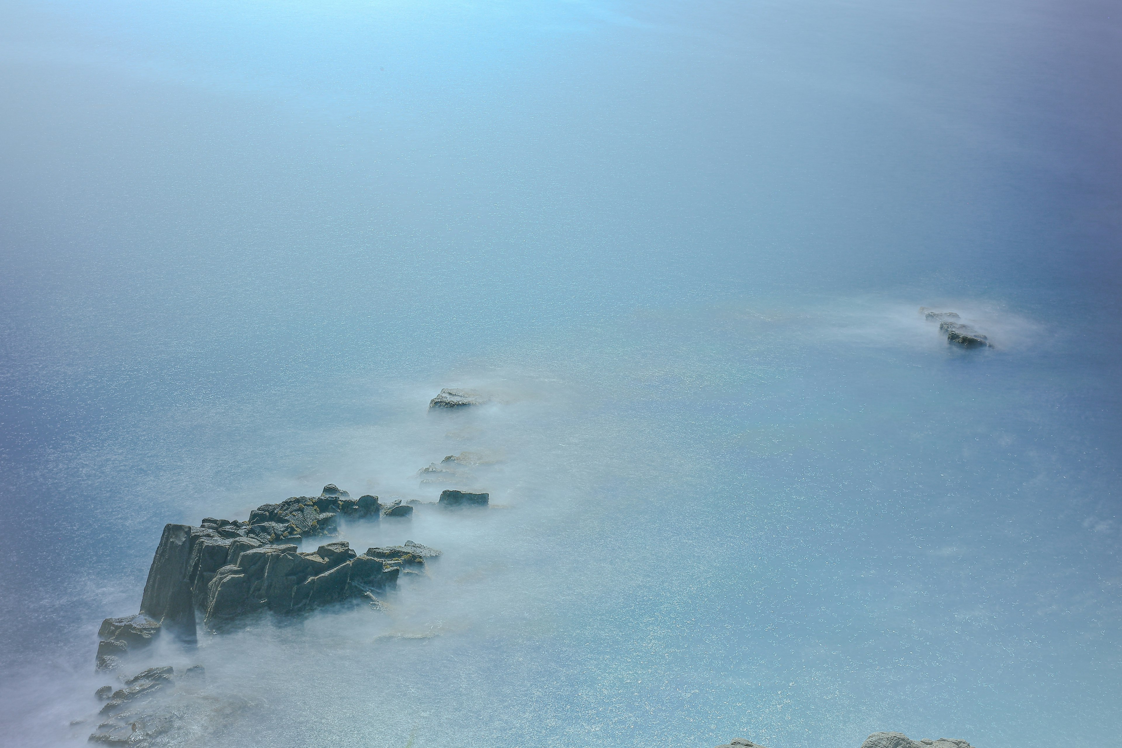 Pemandangan pantai berbatu dengan kabut di atas lautan biru