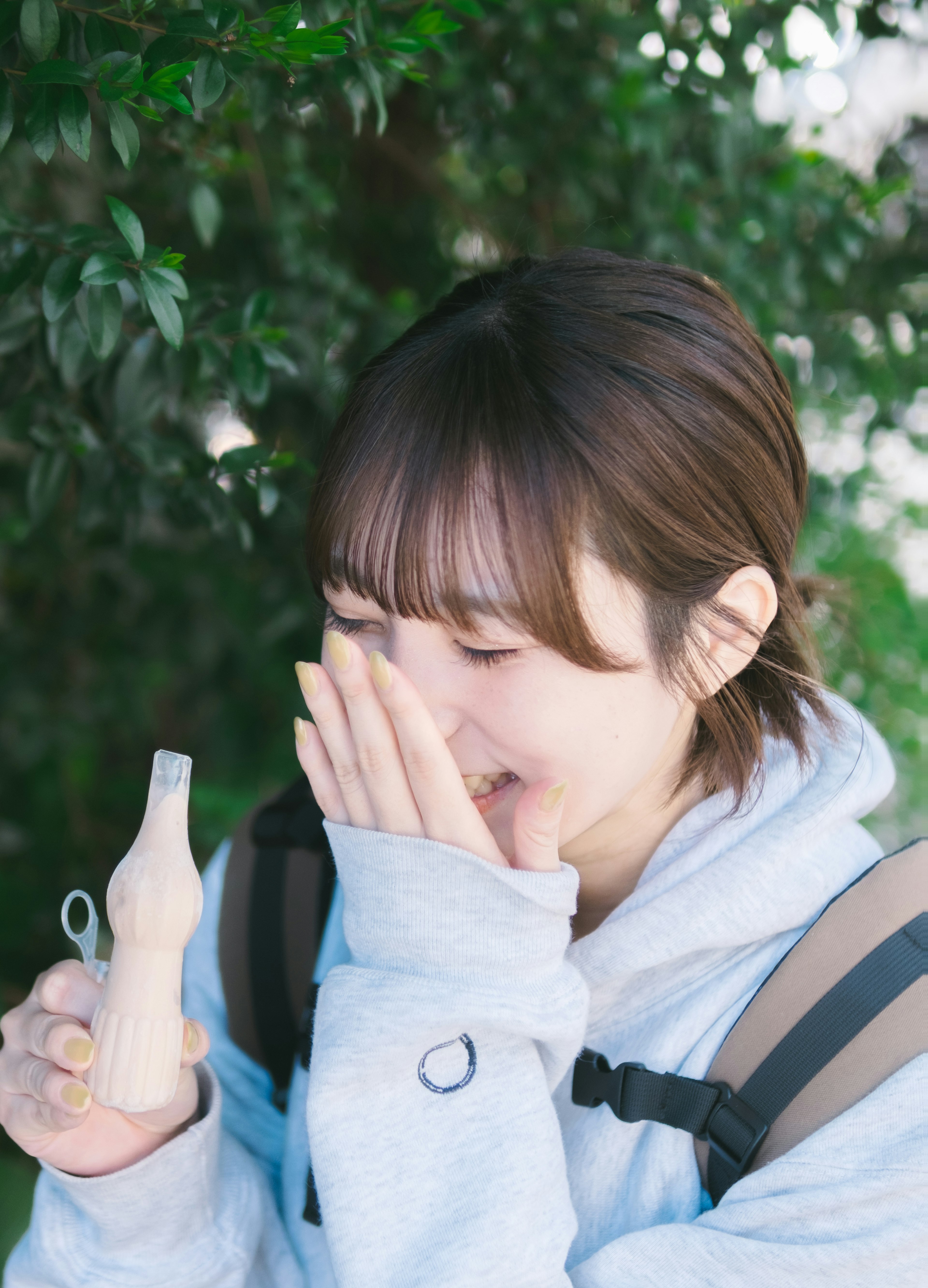 年轻女性微笑着用手捂住脸旁边有绿色植物