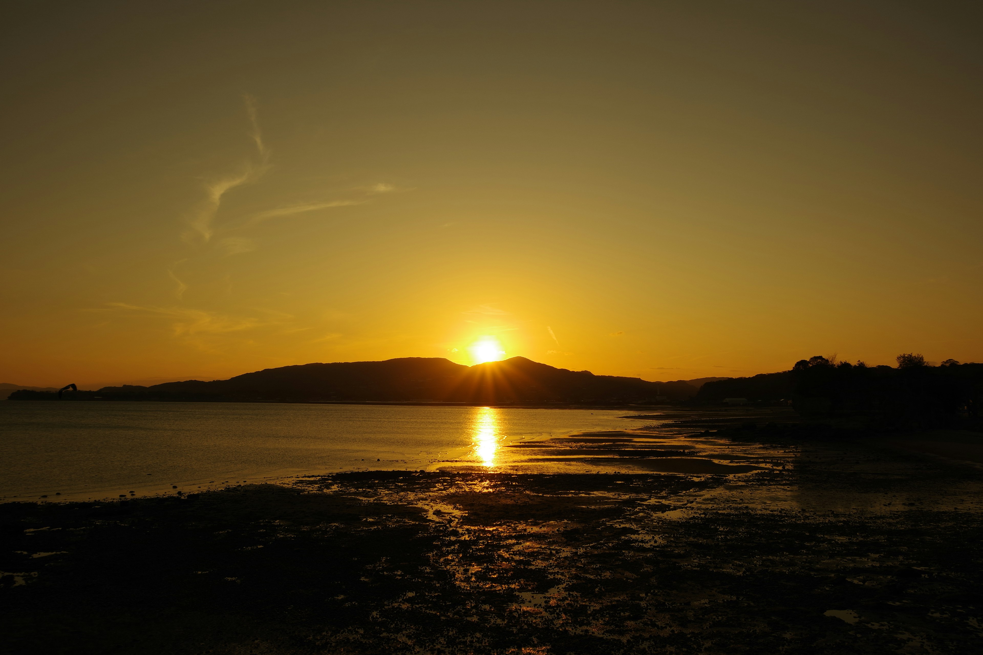 Puesta de sol sobre un mar tranquilo con siluetas de colinas