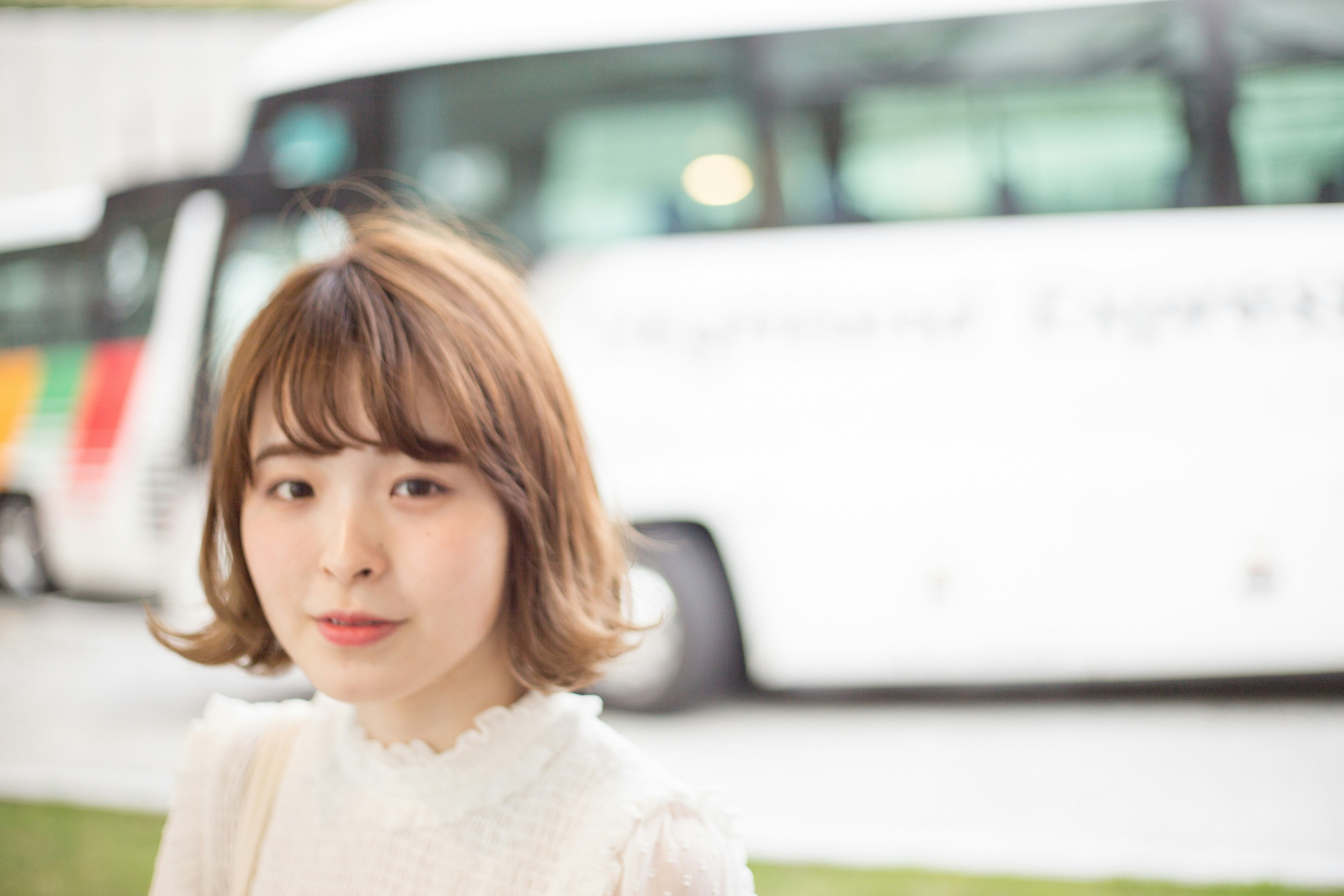 Porträt einer jungen Frau in einem weißen Oberteil mit einem Bus im Hintergrund