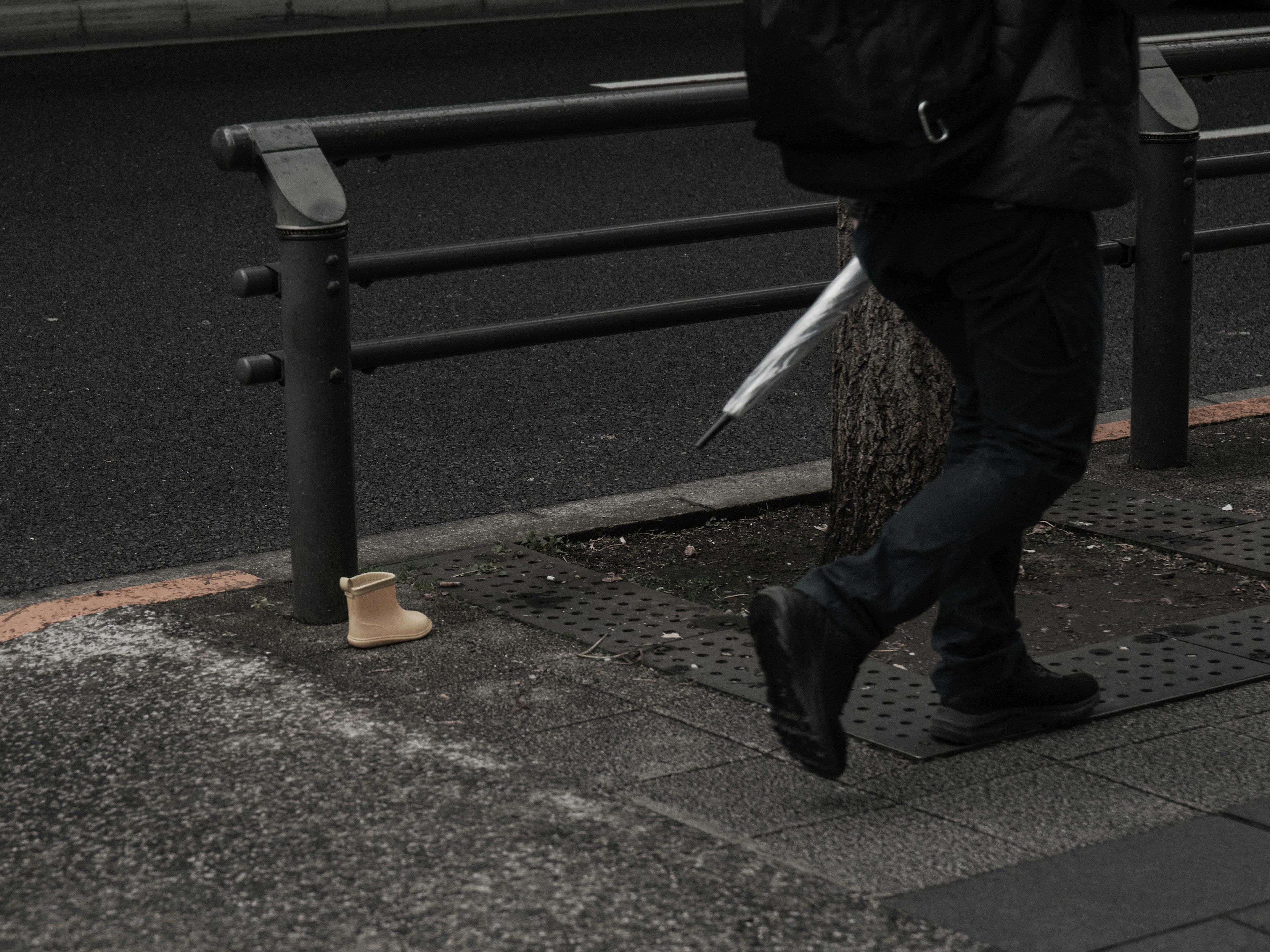 Una persona caminando con un paraguas y un zapato colocado en el suelo